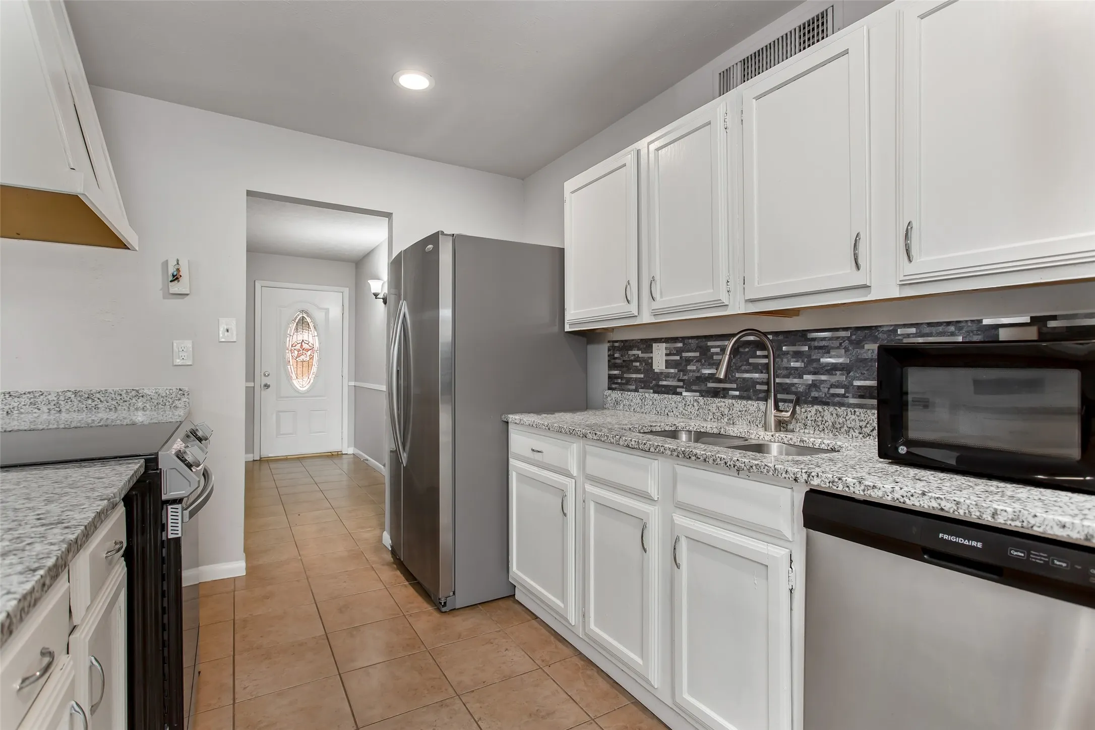 Kitchen featuring white cabinetry, light-toned countertops, tile flooring, and stainless steel appliances