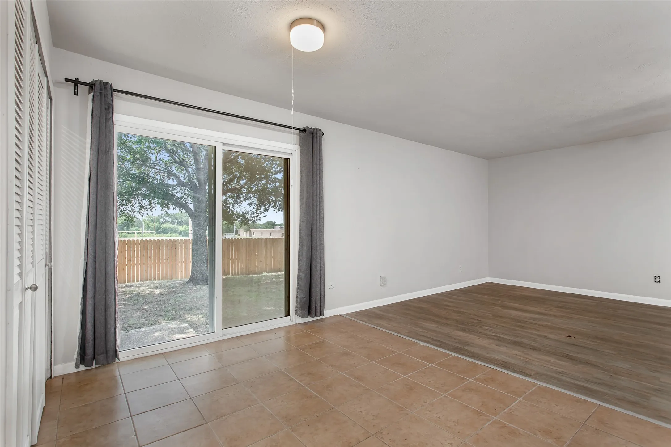 Sliding glass door leading to the backyard, light tile flooring, wood-finish flooring, white walls, and a ceiling-mounted light fixture