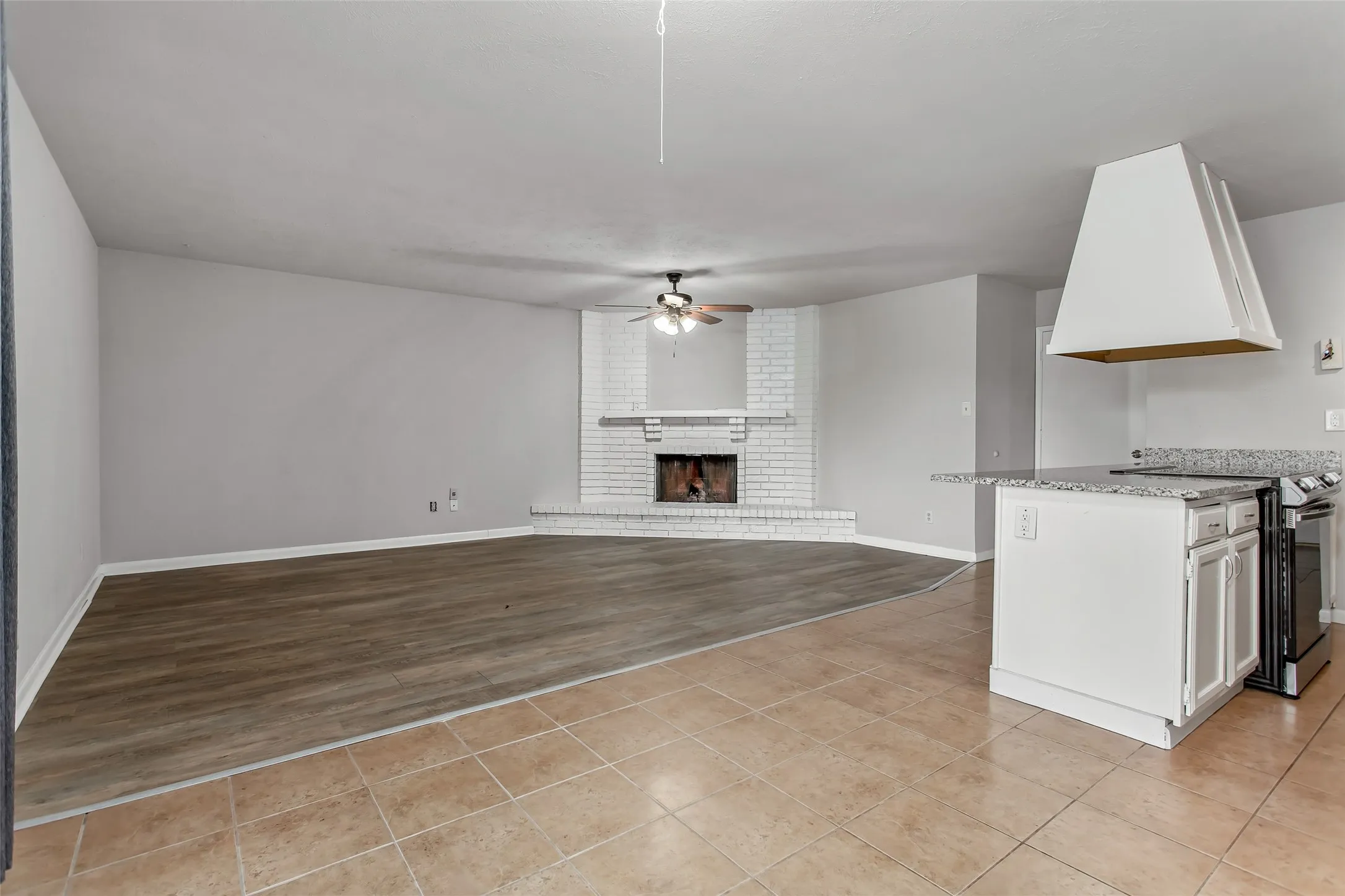 Living area with wood-finish flooring, a white brick fireplace, and a ceiling fan