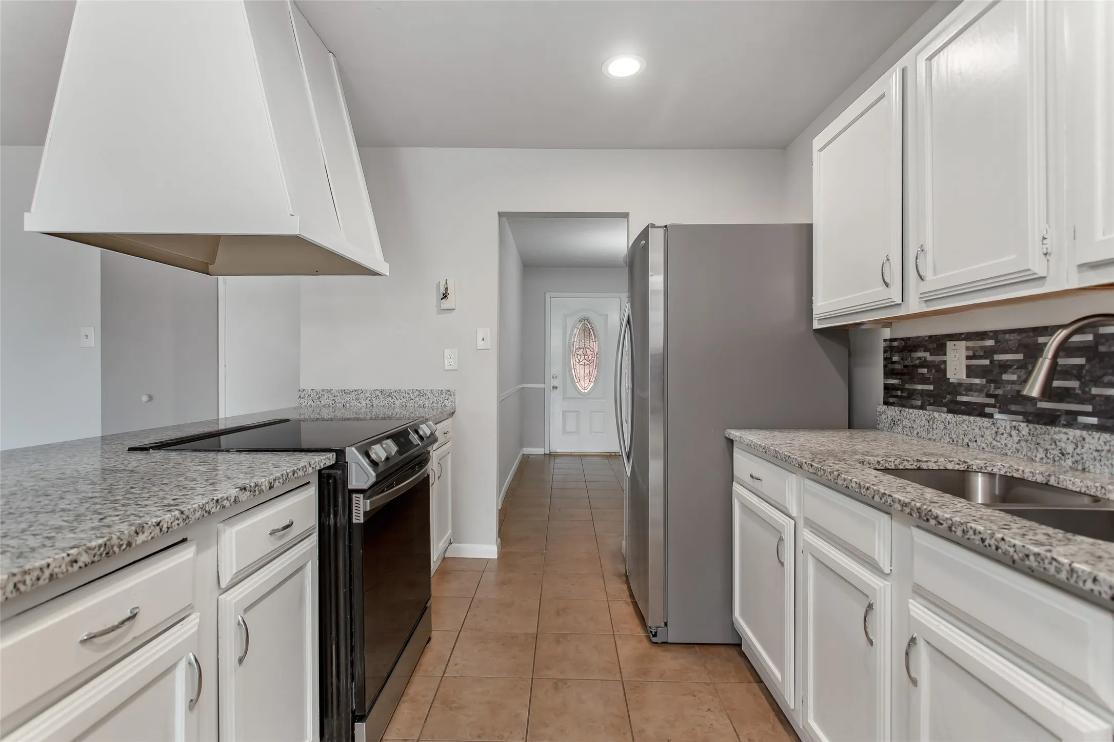 Kitchen featuring white cabinetry, light-toned countertops, a stainless steel sink, tile backsplash, and a built-in electric range