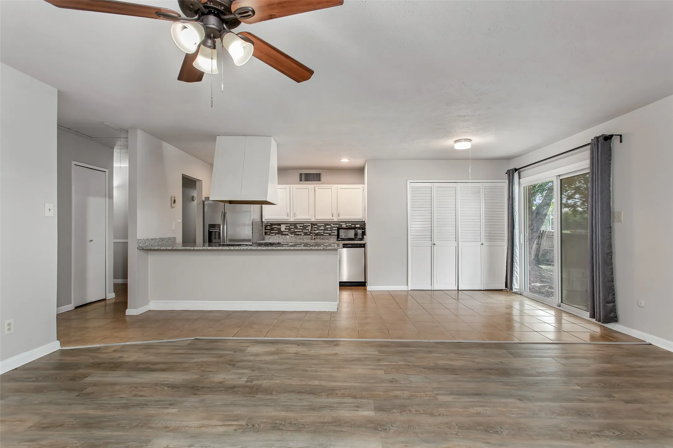 Wood-finish flooring, tiled kitchen flooring, kitchen island with granite-style countertop, white cabinetry, and sliding glass door