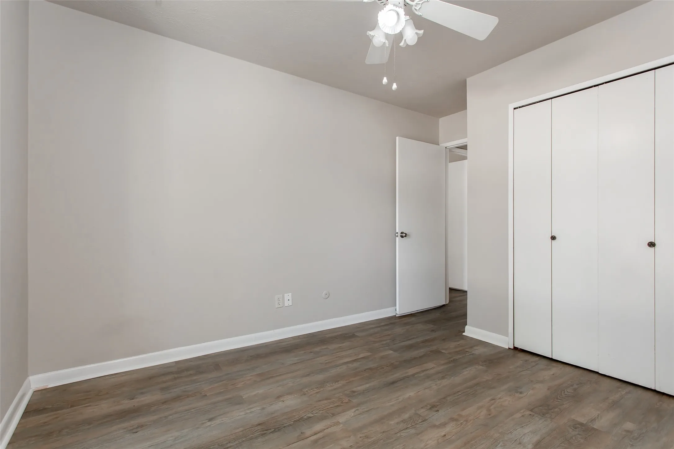 Wood-finish flooring, light gray walls, white baseboards, and a ceiling fan with light fixture
