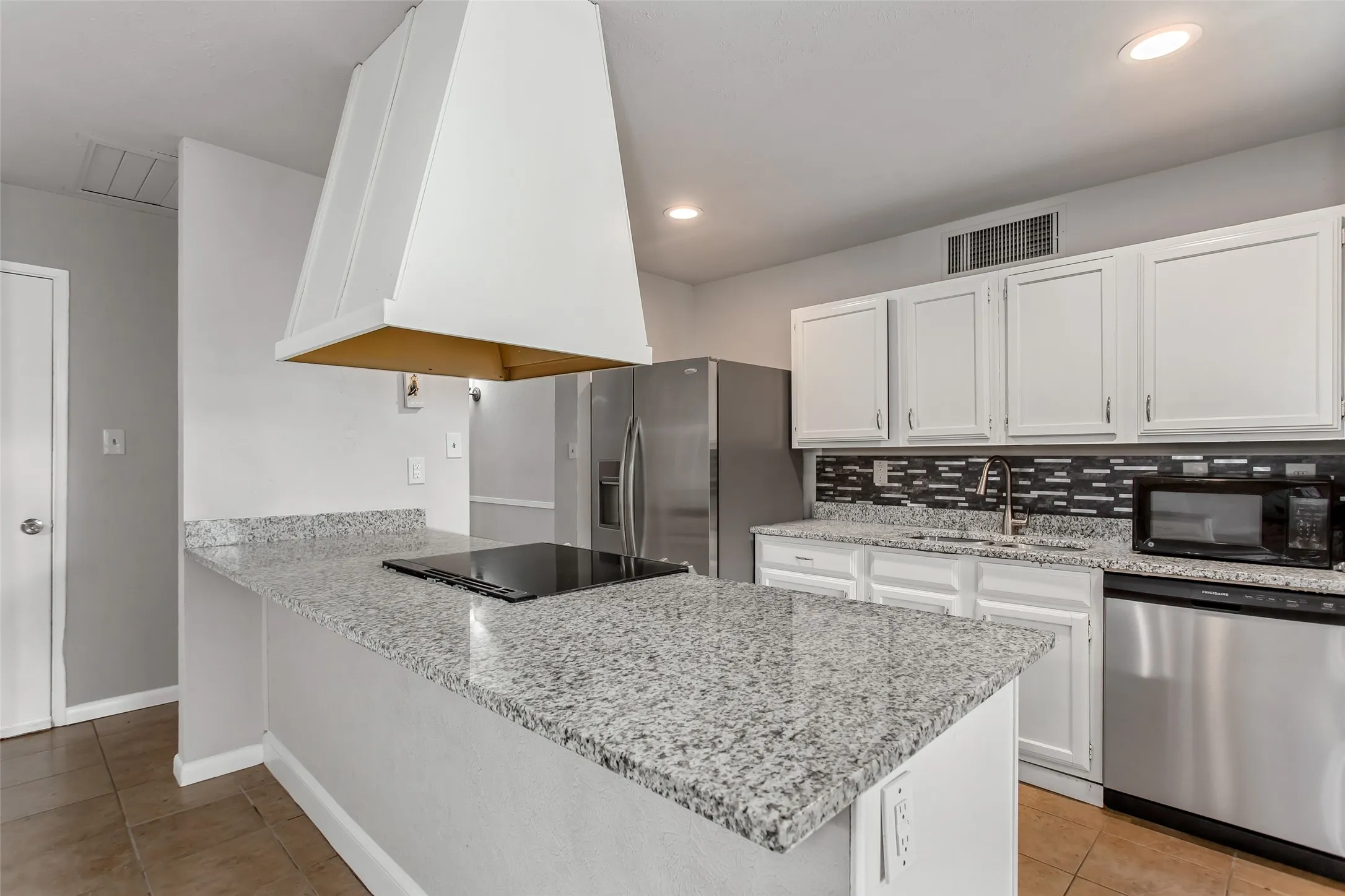 Kitchen featuring a spacious island, built-in cooktop, and a decorative range hood