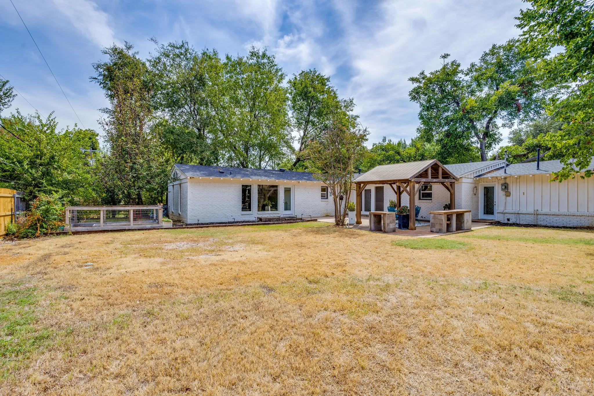 Expansive backyard with a covered patio structure, white exterior siding, and a wooden fence