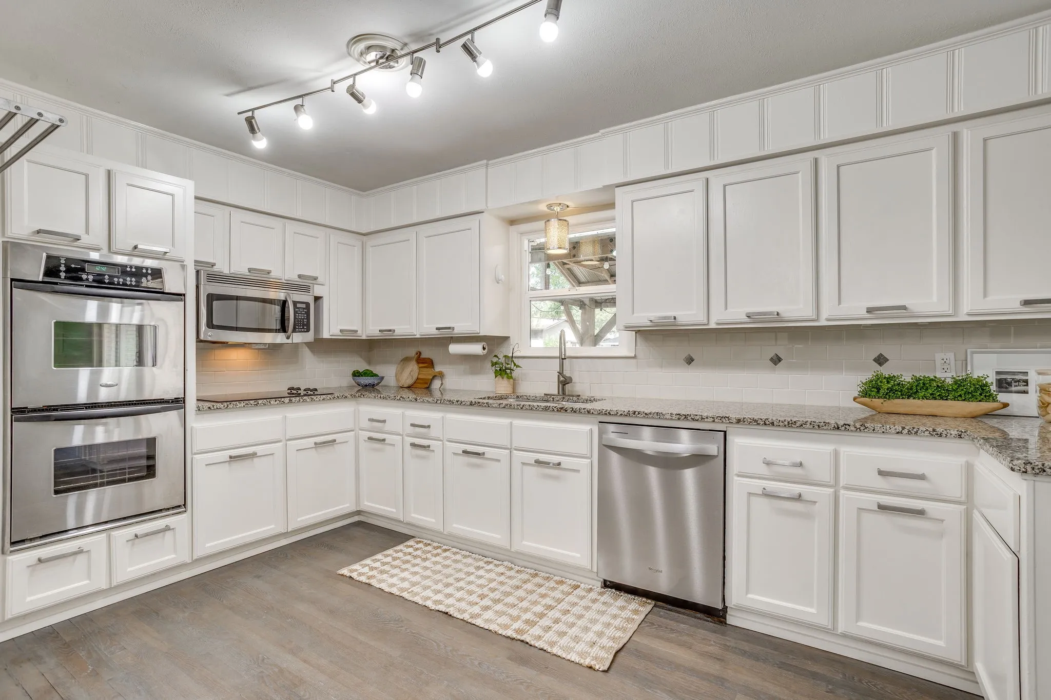 White cabinetry with stainless steel appliances, speckled countertops, and tile backsplash