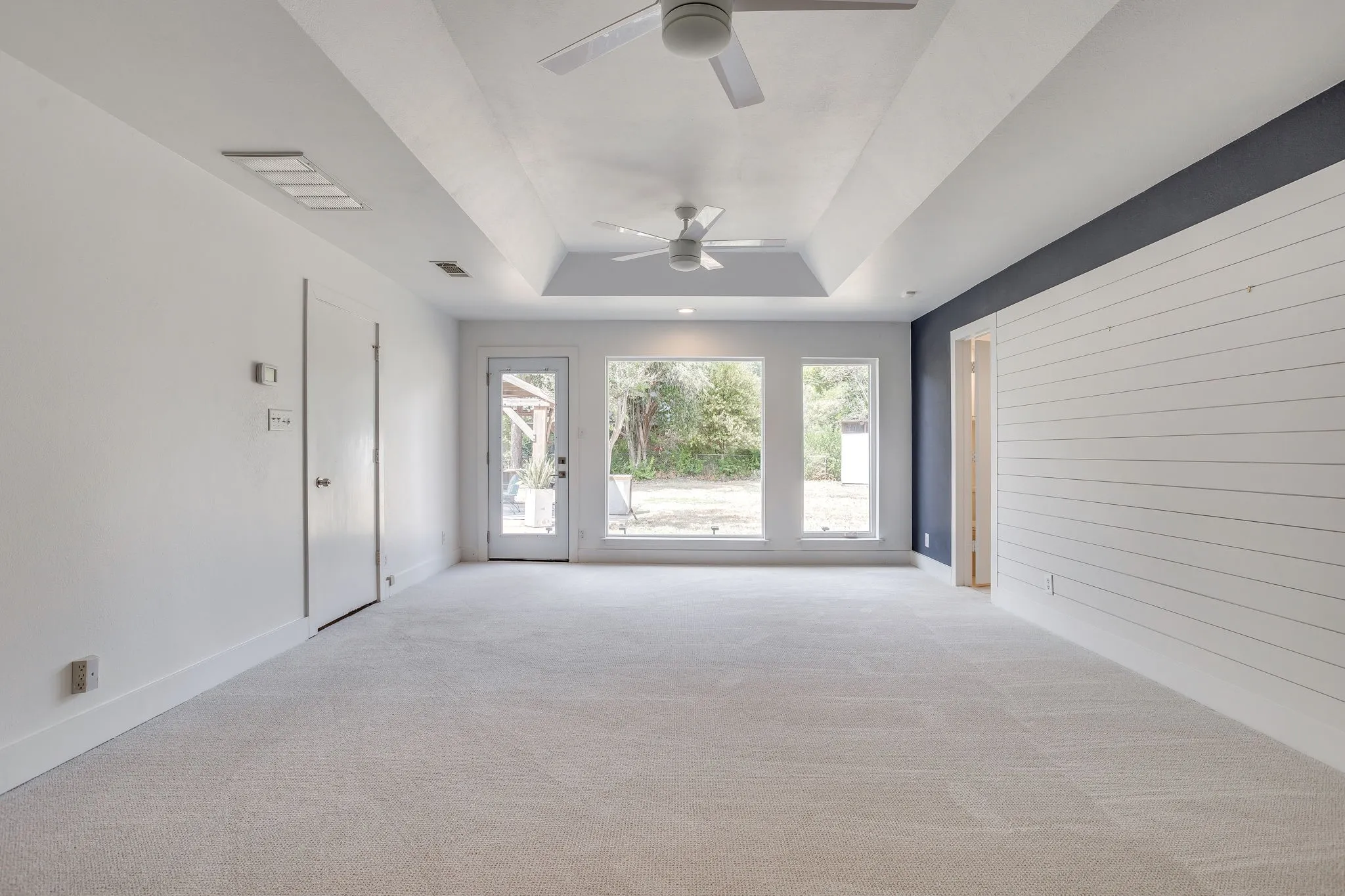 Tray ceiling, recessed lighting, ceiling fan, shiplap accent wall, and multiple windows