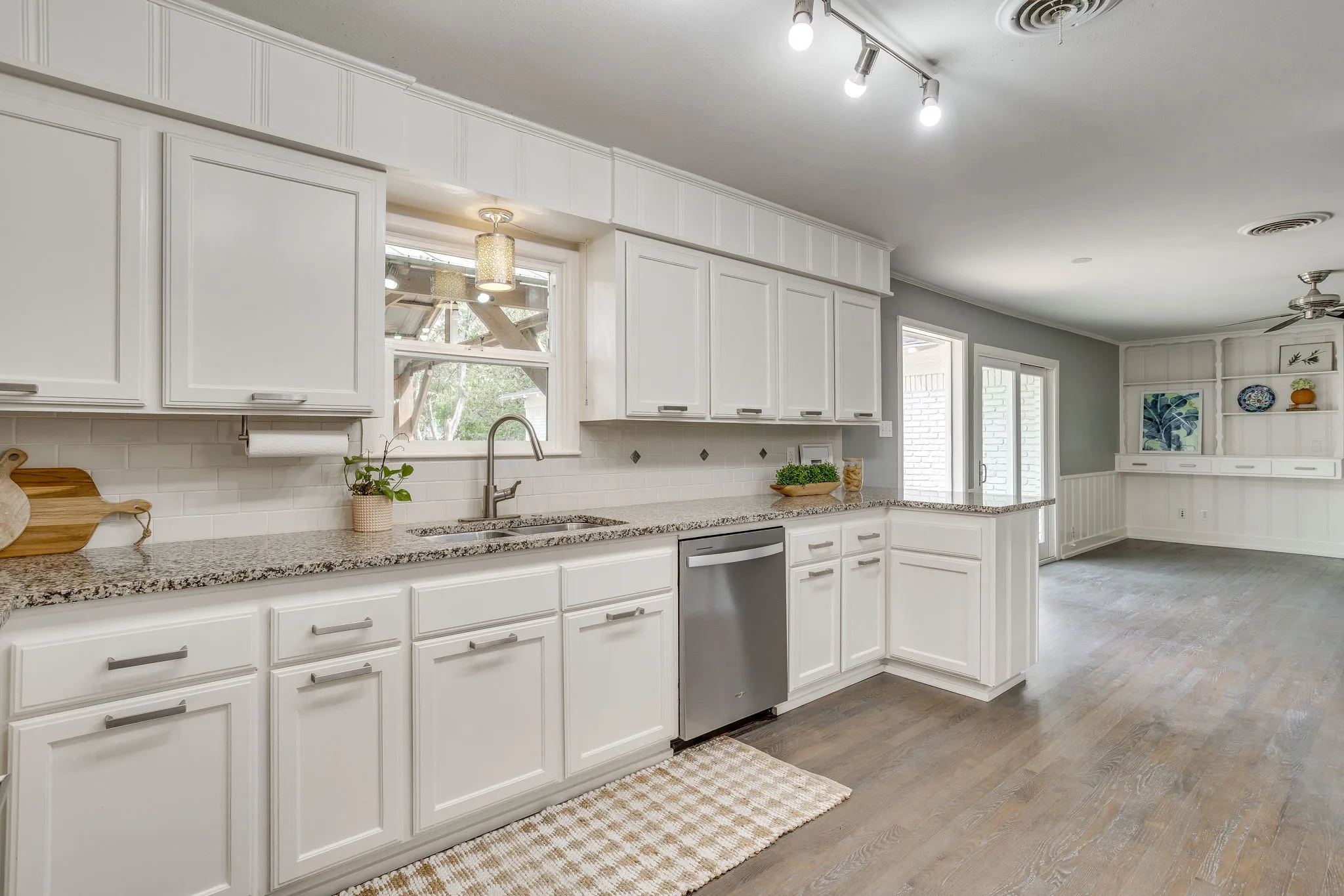 White shaker-style cabinetry with brushed nickel hardware, speckled countertops, stainless steel dishwasher, white subway tile backsplash, and wood-finish flooring