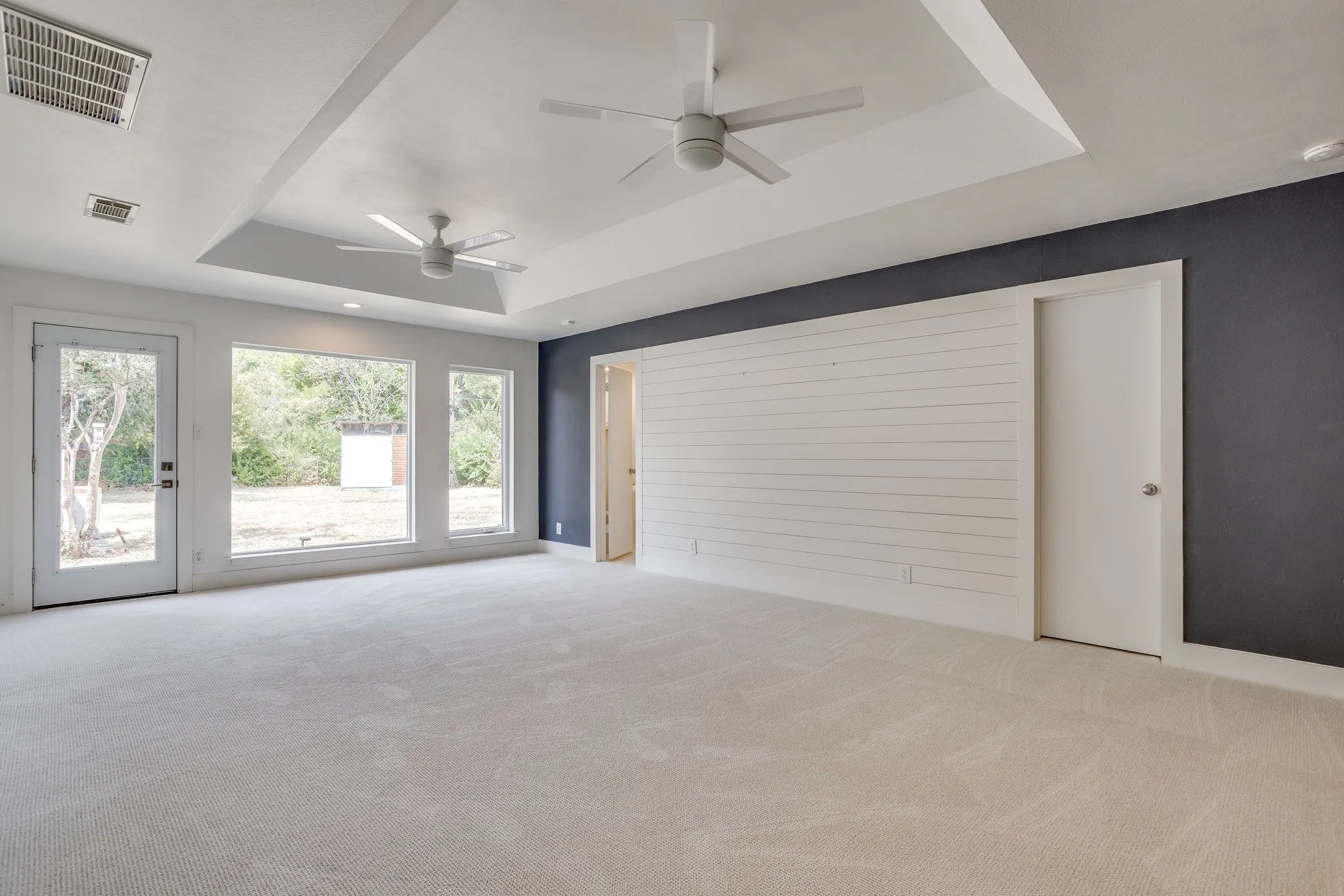 Recessed ceiling with two ceiling fans, shiplap accent wall, dark accent wall, and light-toned carpeting