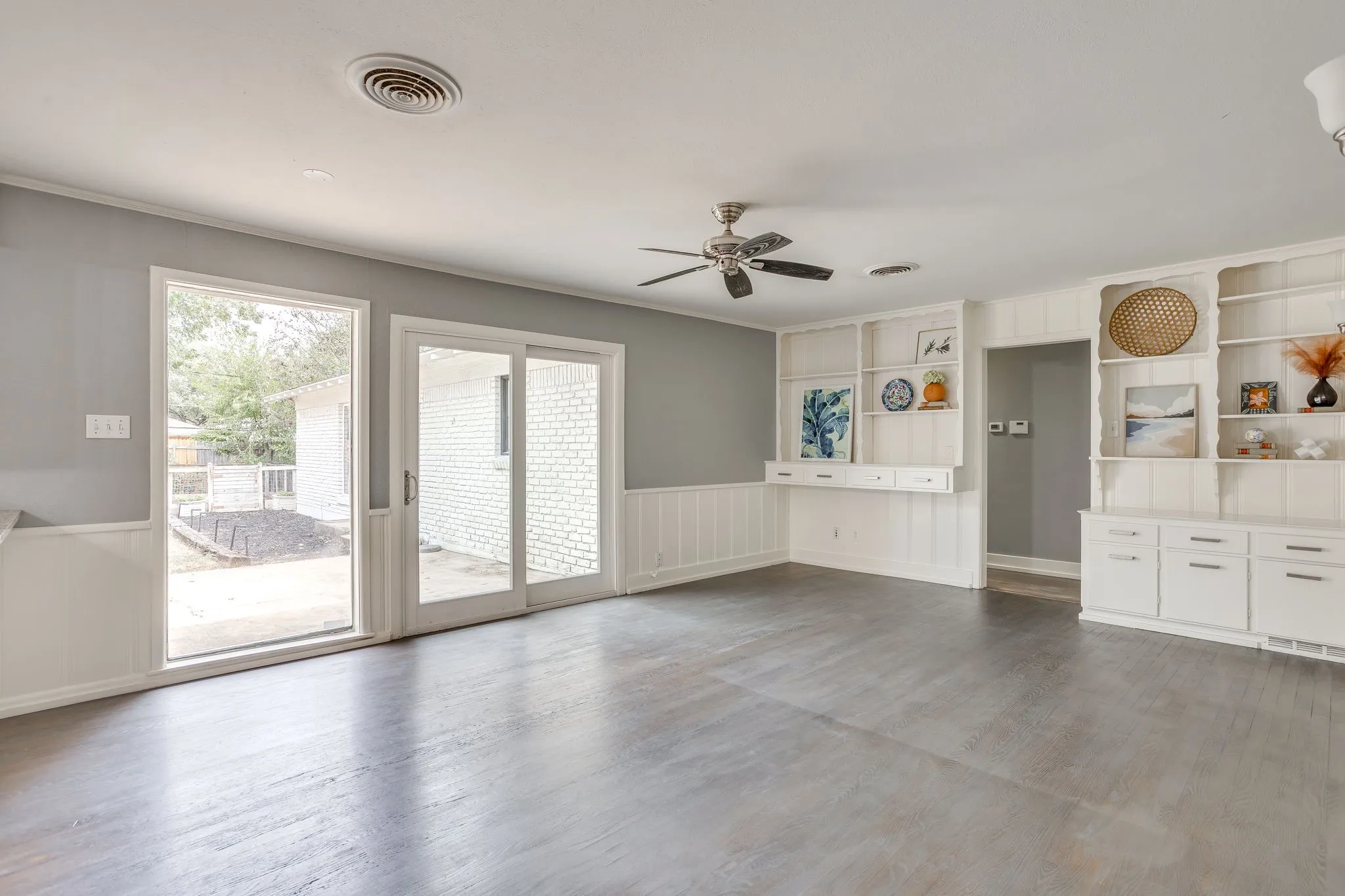 Wood-finish flooring, built-in shelving, white wainscoting, ceiling fan, and sliding glass doors