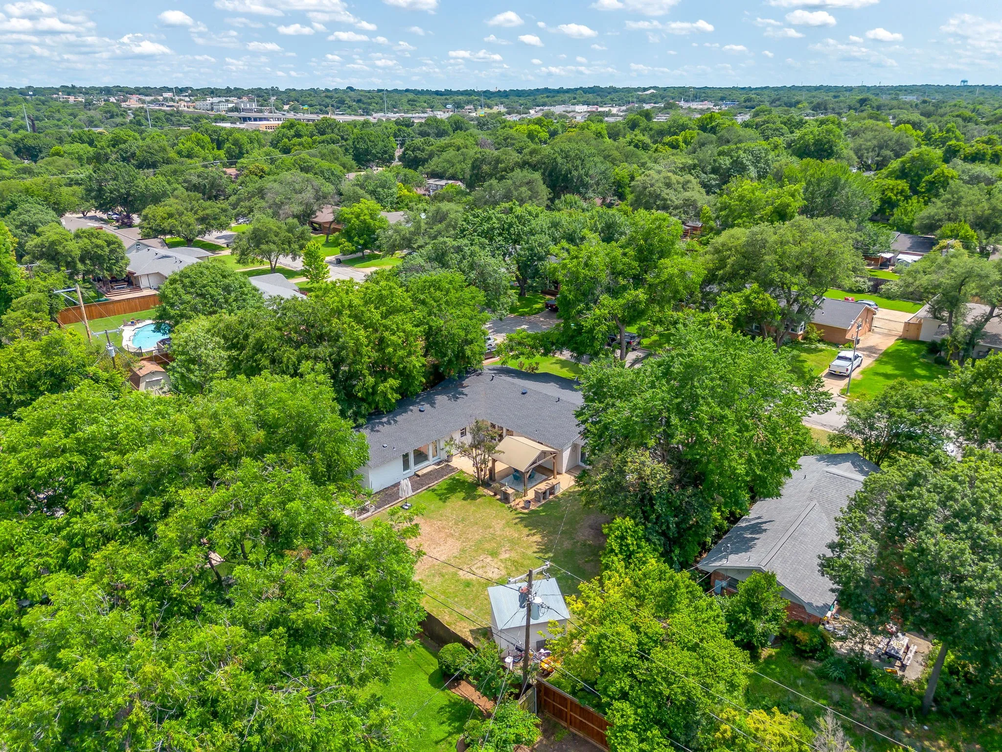 Aerial perspective of a property with an expansive backyard, surrounded by mature trees, and featuring a swimming pool
