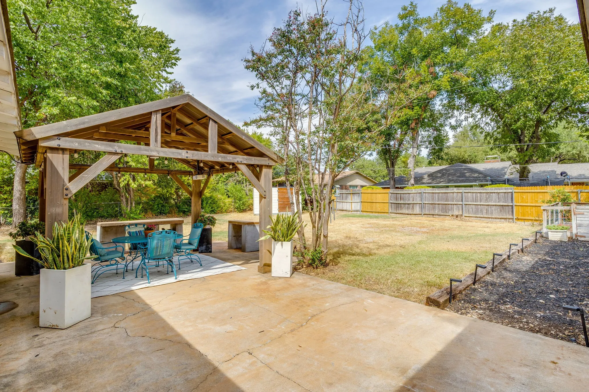 Expansive concrete patio featuring a large wooden gazebo, built-in outdoor counters, and a fenced backyard