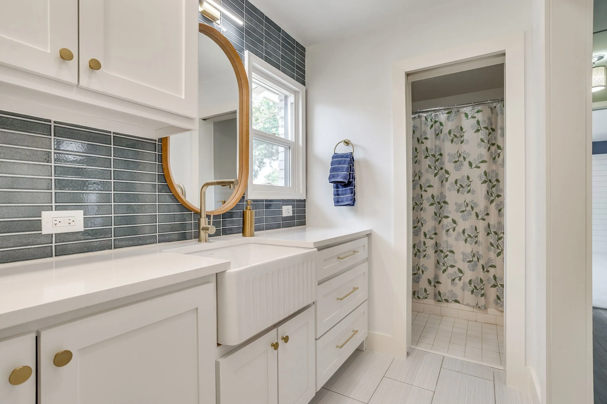 White shaker-style cabinetry with gold-tone hardware, white farmhouse sink, white countertops, and a blue subway tile backsplash
