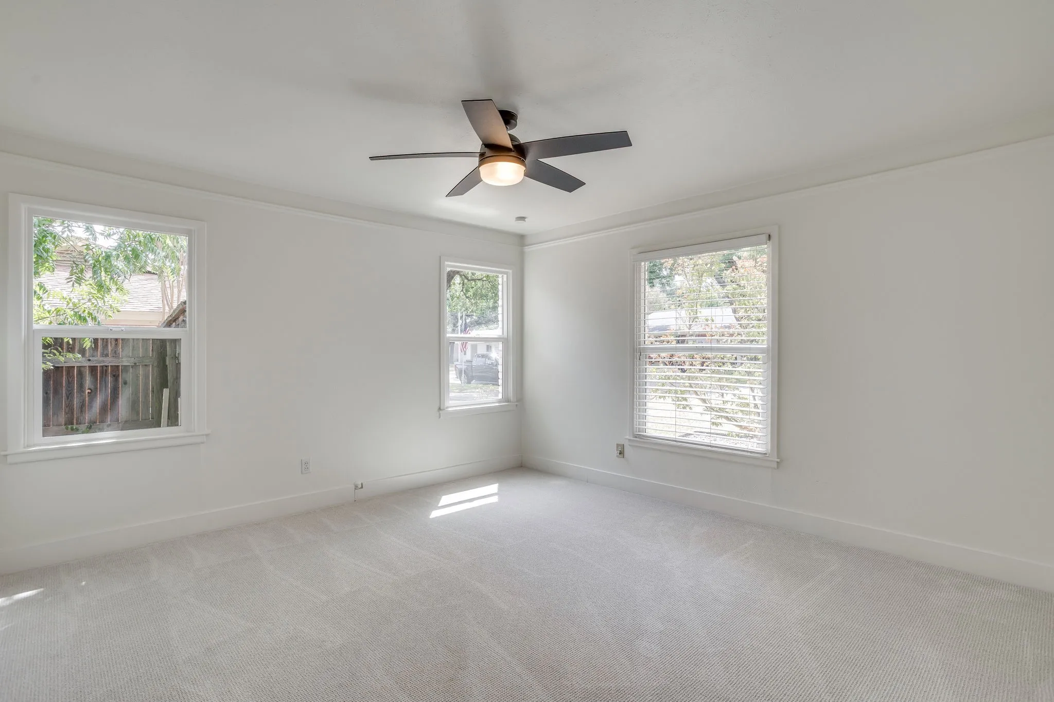 Light gray carpeted flooring, white walls, two white-framed windows with blinds, and a ceiling fan with integrated lighting