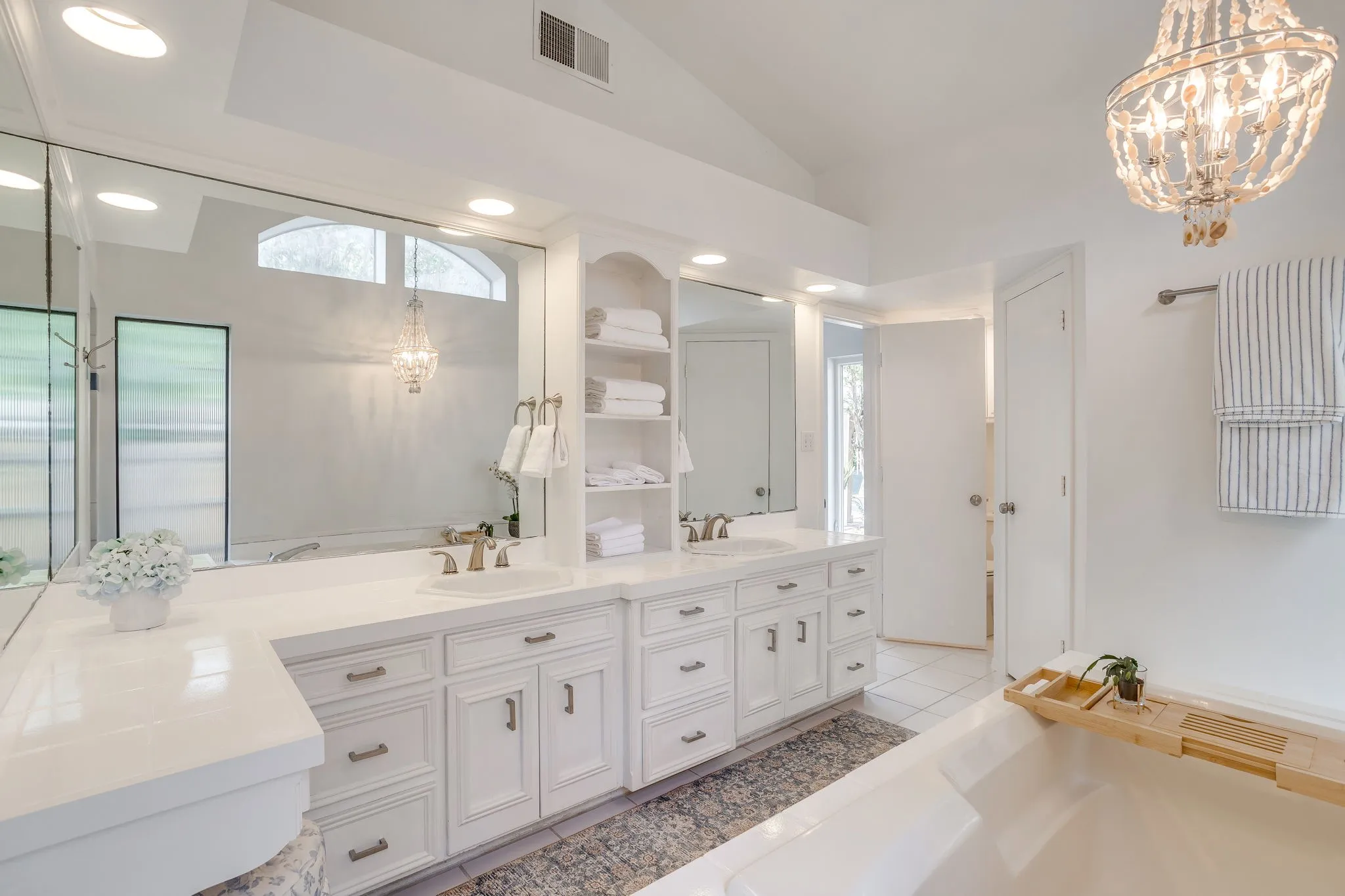 Dual vanity with white cabinetry, mirrored wall, recessed lighting, built-in shelving, and vaulted ceiling