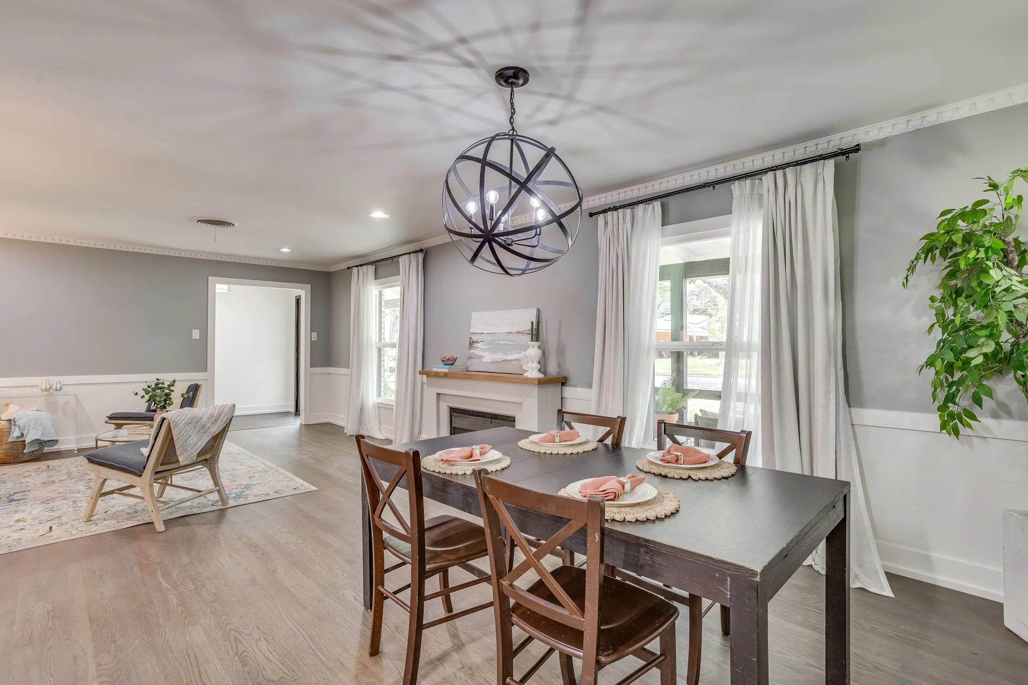 Wood-finish flooring, fireplace with wood mantel, decorative wainscoting, crown molding, and an exposed bulb chandelier