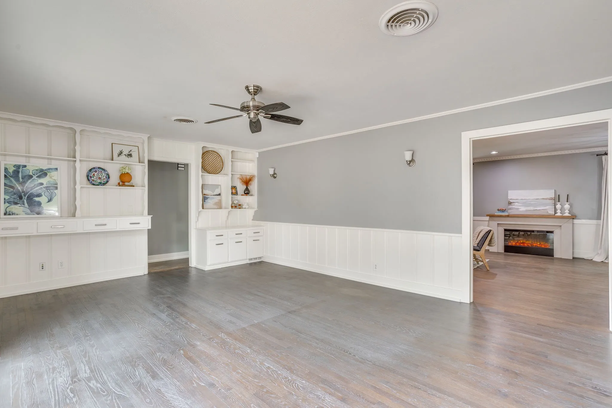 Wood-finish flooring, built-in shelving, ceiling fan with light fixture, and wainscoting
