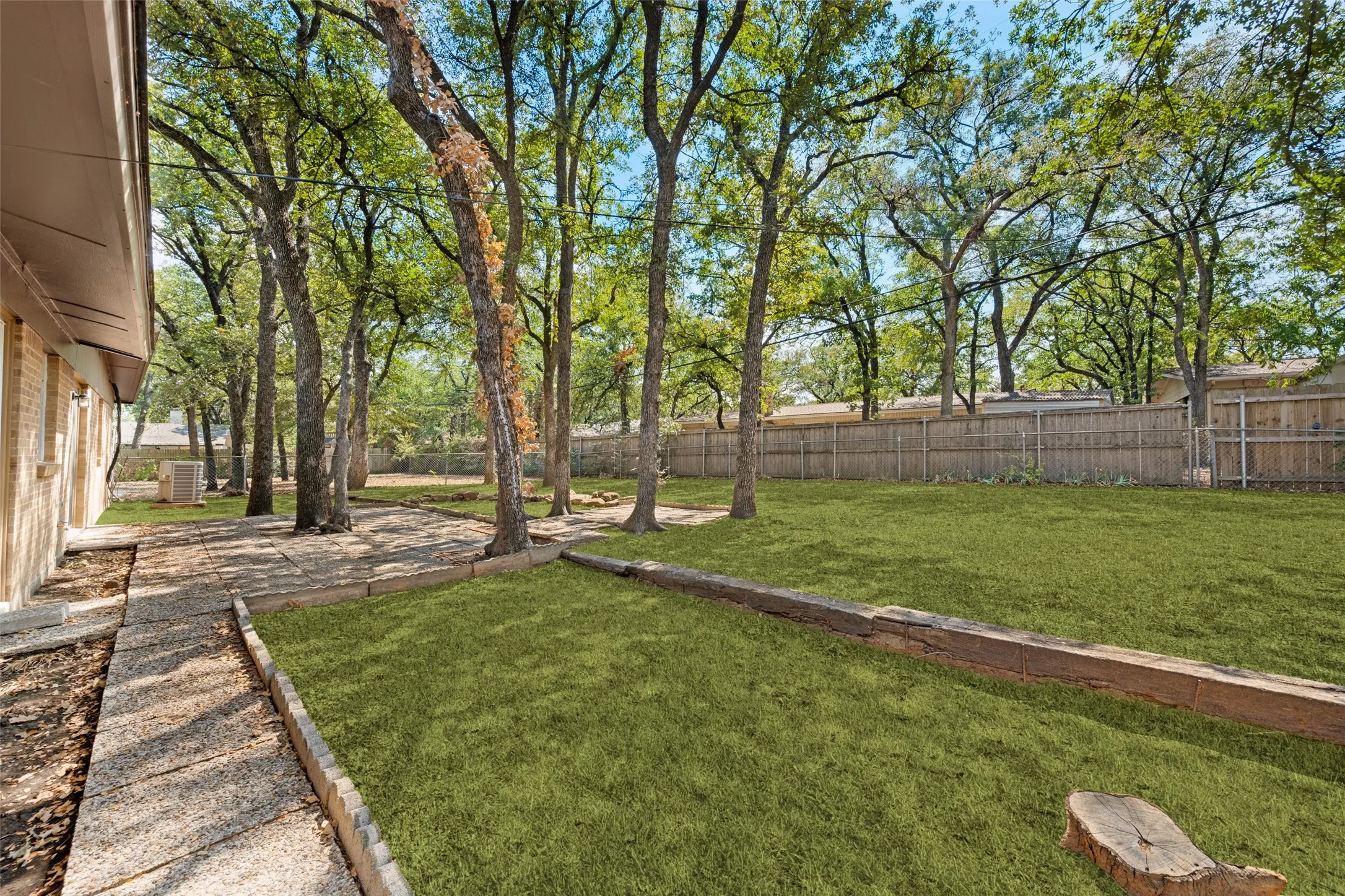 Expansive backyard featuring a lush lawn, mature trees, wood retaining walls, and a perimeter privacy fence