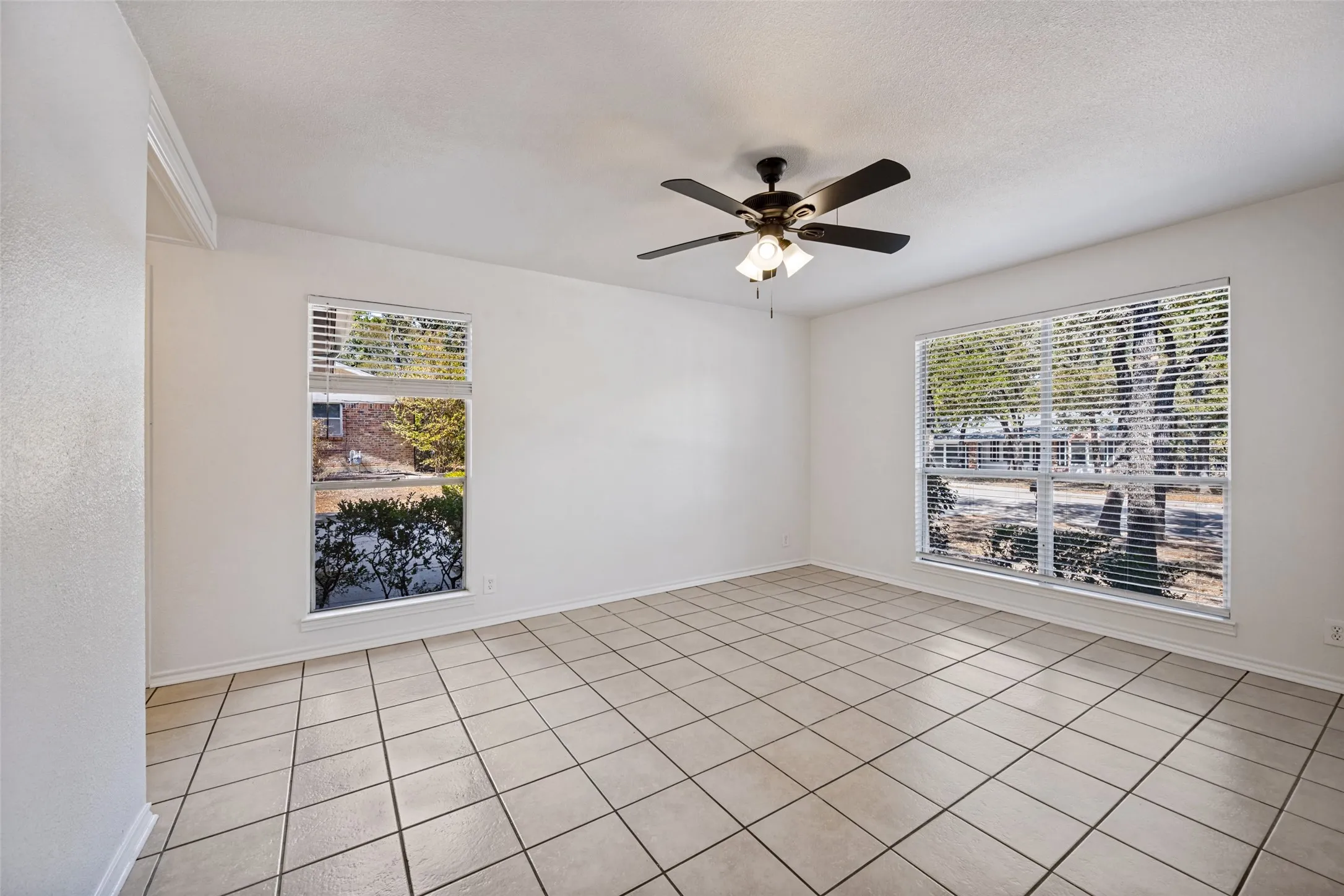 Spacious room featuring neutral tile flooring, white walls, and a ceiling fan with integrated lighting