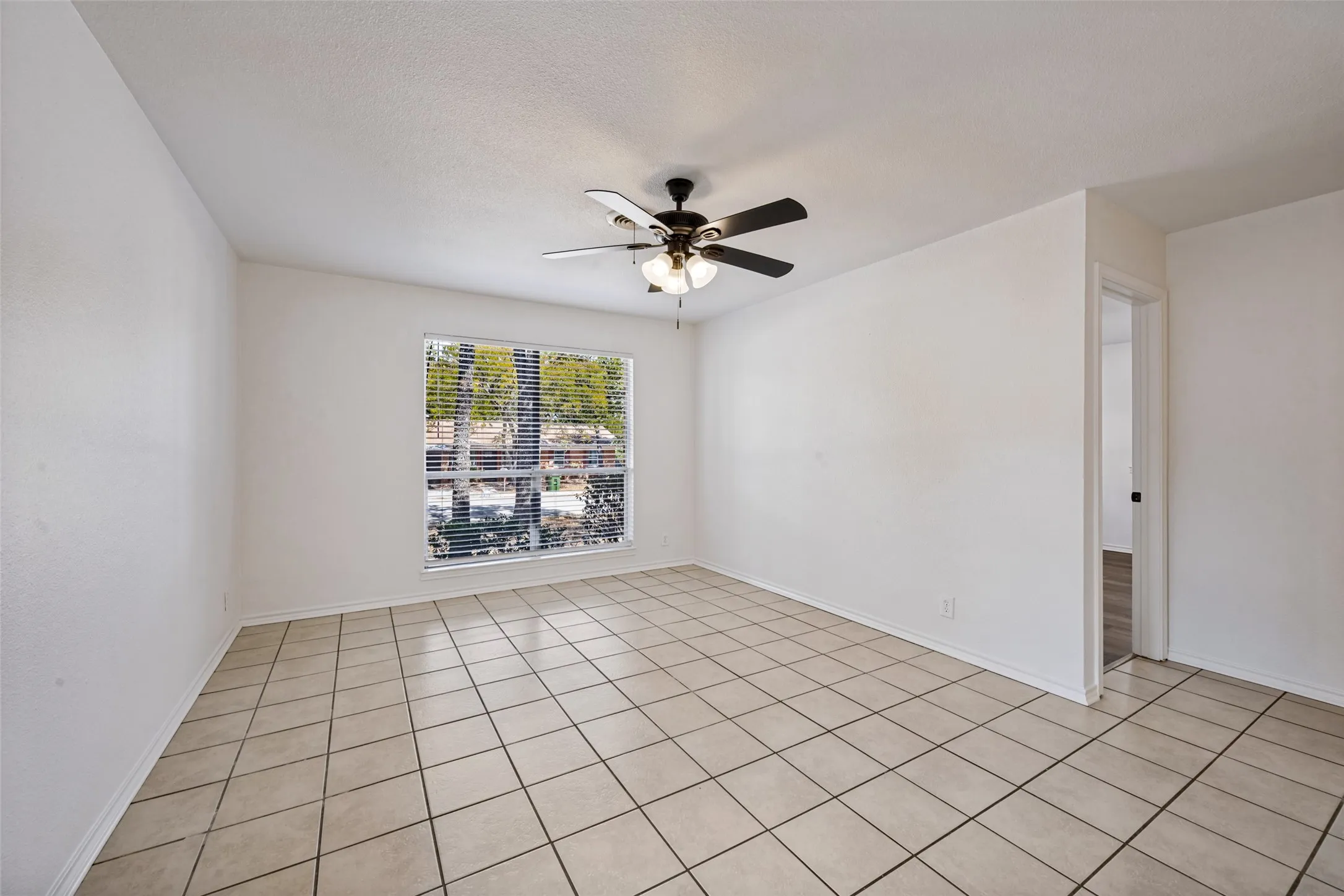 Ceramic tile flooring, large window with blinds, ceiling fan with integrated lighting, and a neutral color palette