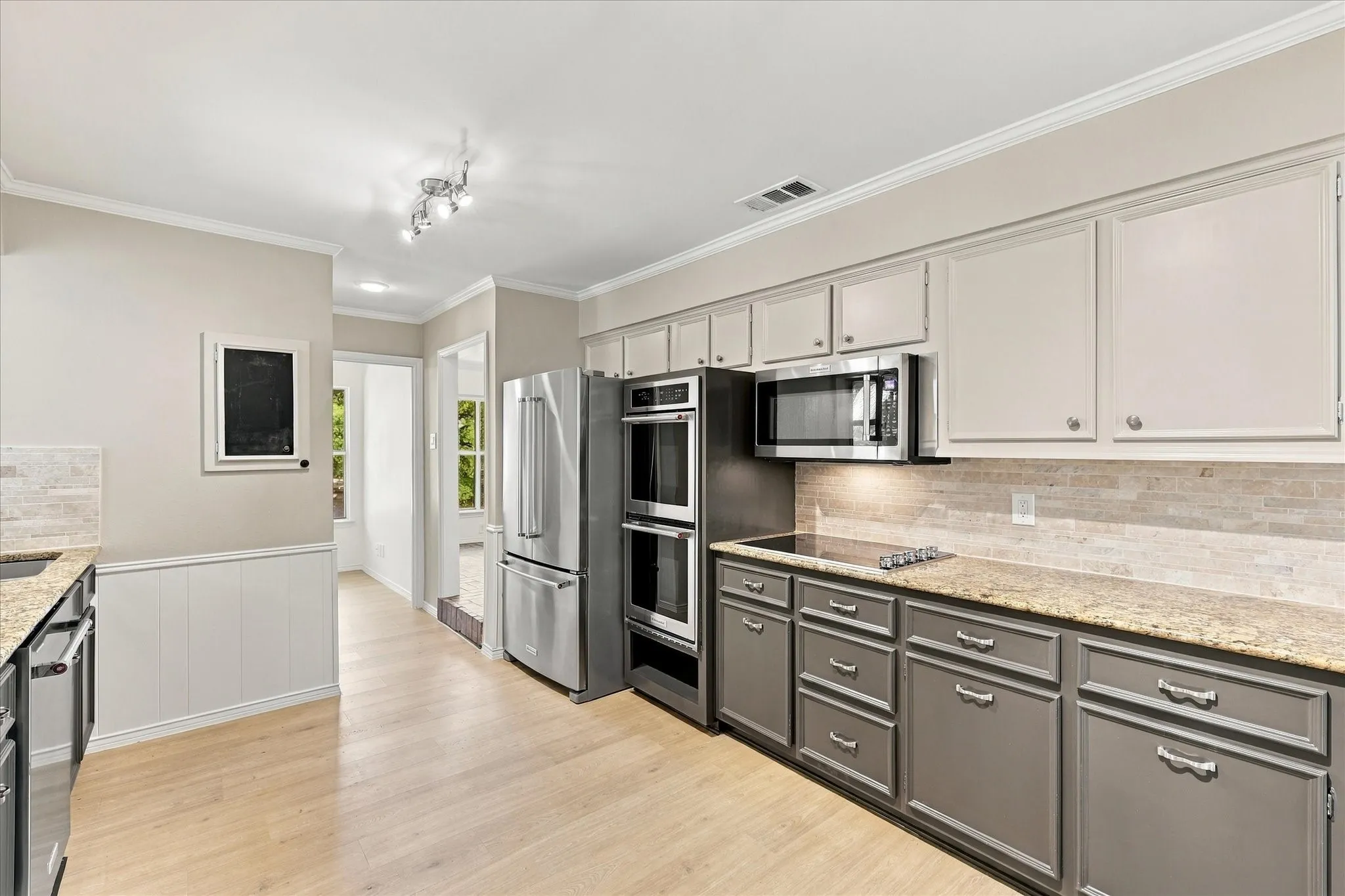 Light wood-finish flooring, stainless steel appliances, two-tone cabinetry, stone countertops, and a tiled backsplash