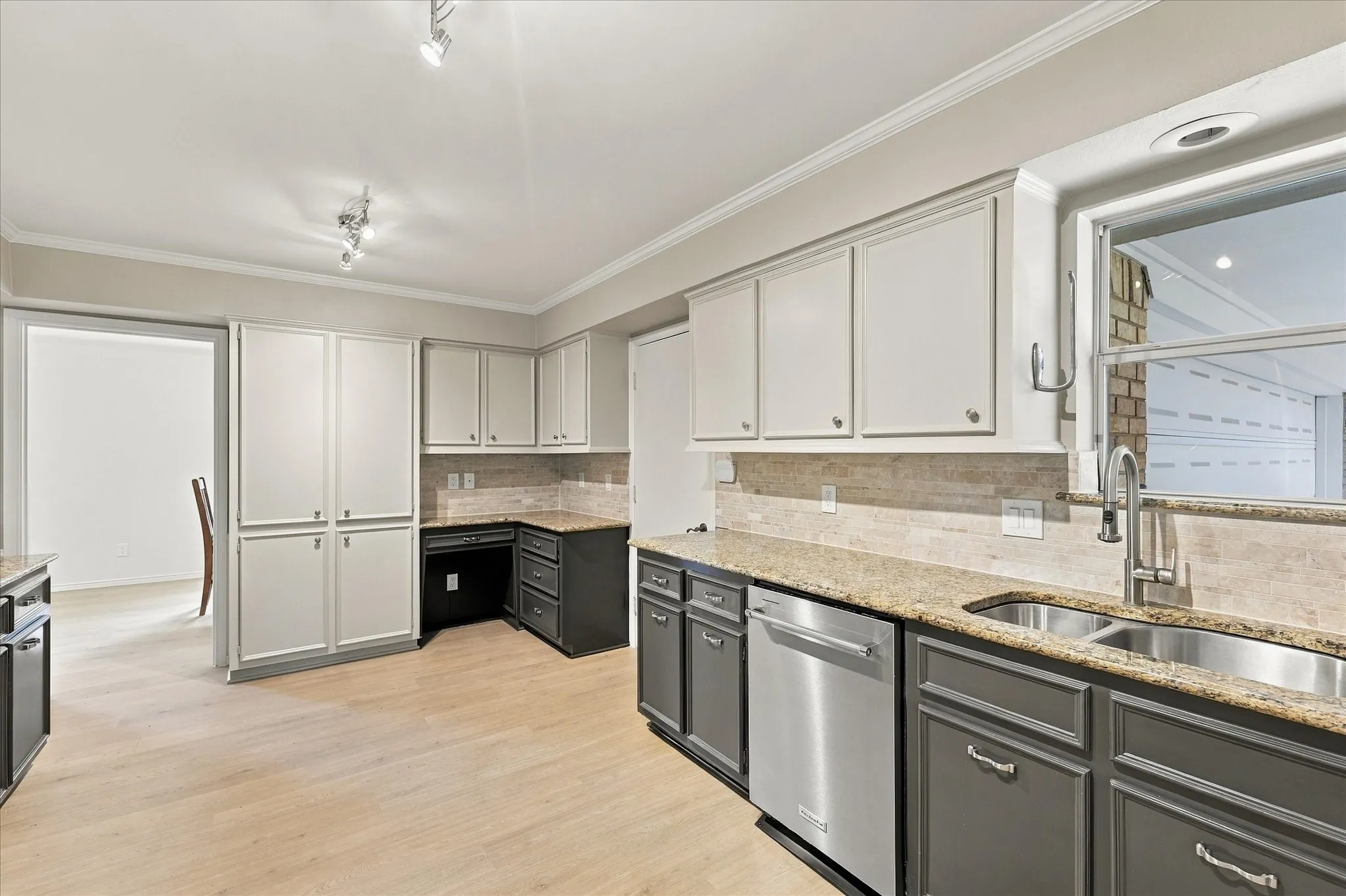 Kitchen featuring light wood-finish flooring, two-tone cabinetry, granite countertops, stone backsplash, and stainless steel appliances