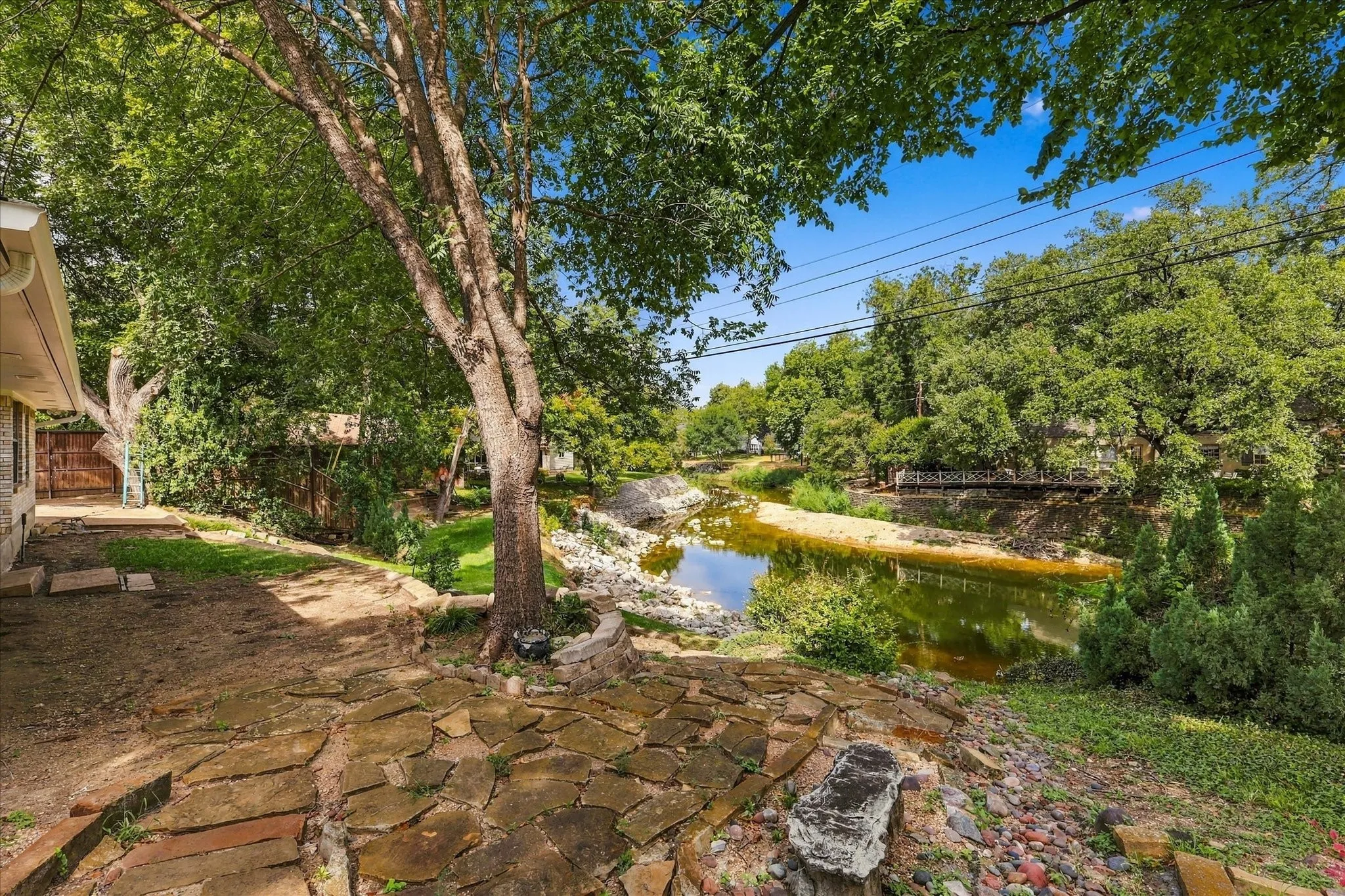 Stone patio with a natural rock edge, mature trees, and a bordering water feature