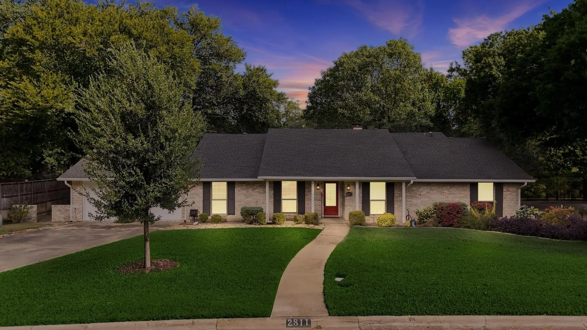 Brick exterior with dark shutters, established landscaping, and a curved concrete walkway