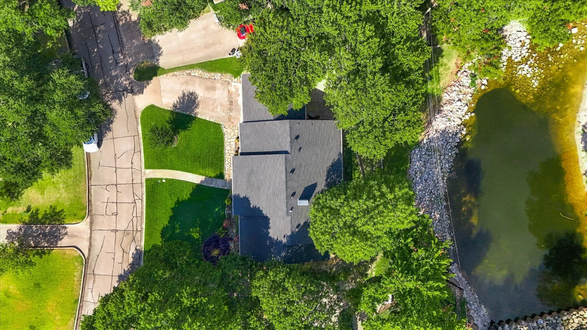 Manicured lawn with mature trees, paved driveways, and a river frontage with stone-lined banks