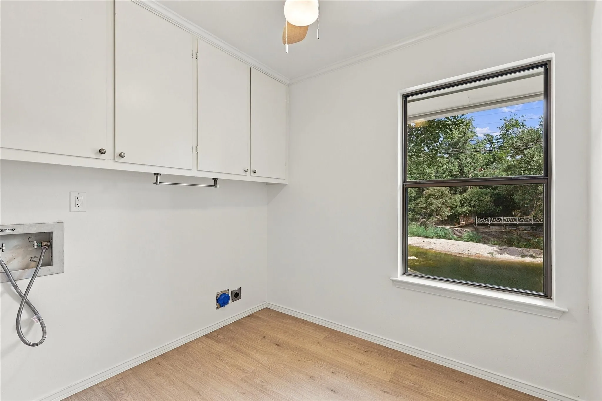 Wood-finish flooring, white cabinetry, and a window with a natural backdrop