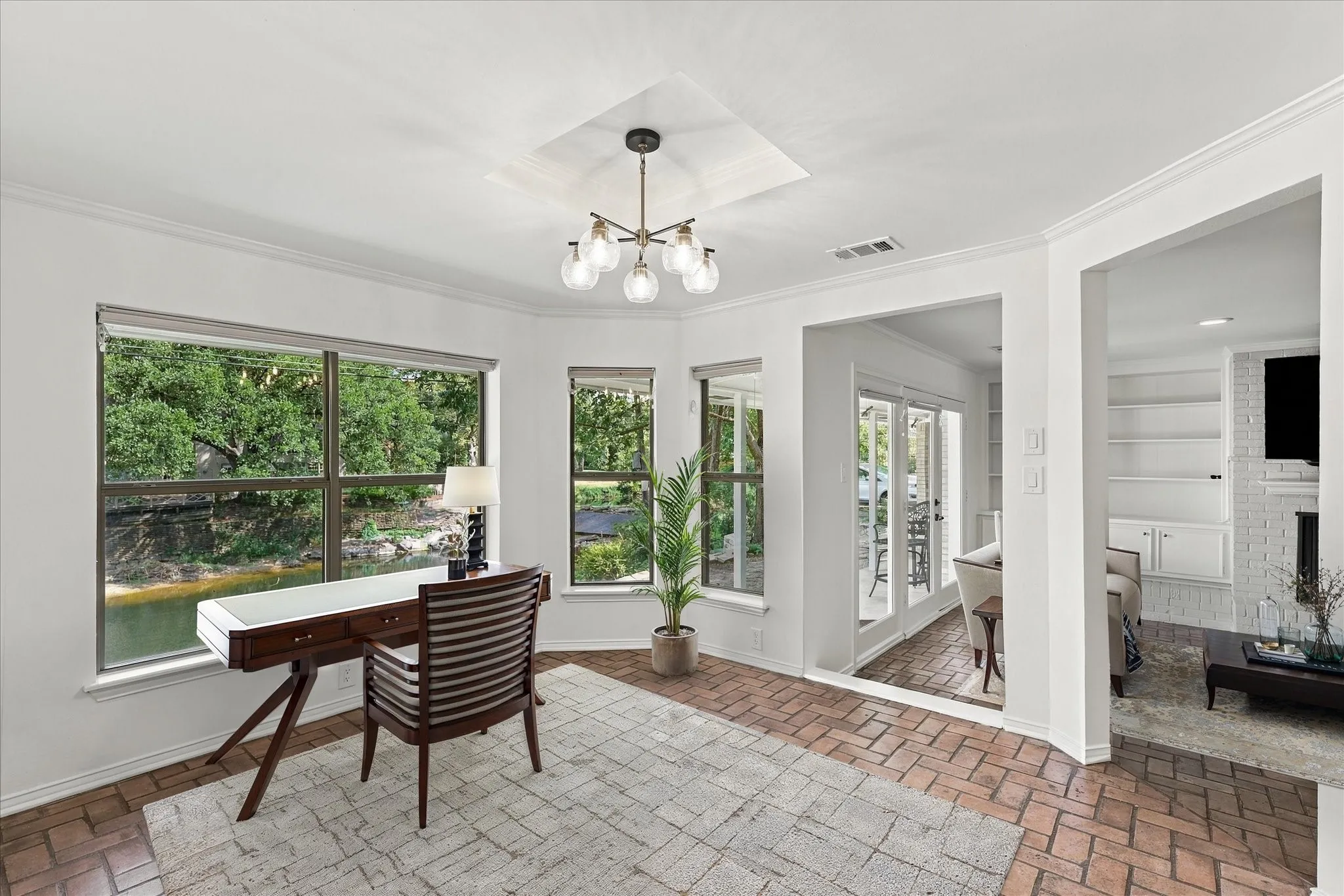 Large windows, recessed ceiling detail, contemporary chandelier, brick-finish flooring, white built-in shelving