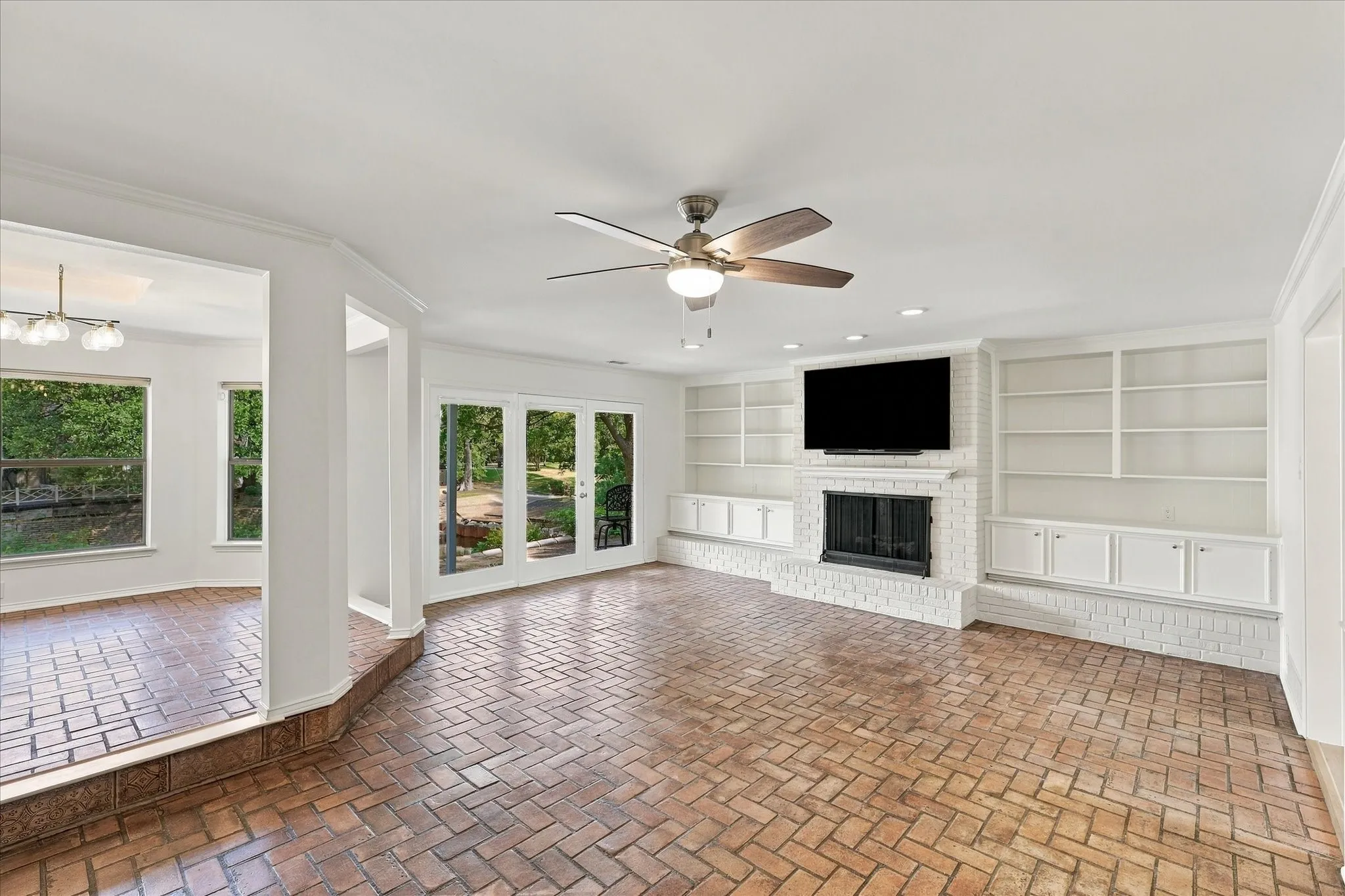 Herringbone brick flooring, white brick fireplace with hearth, built-in shelving, built-in cabinetry, and French doors