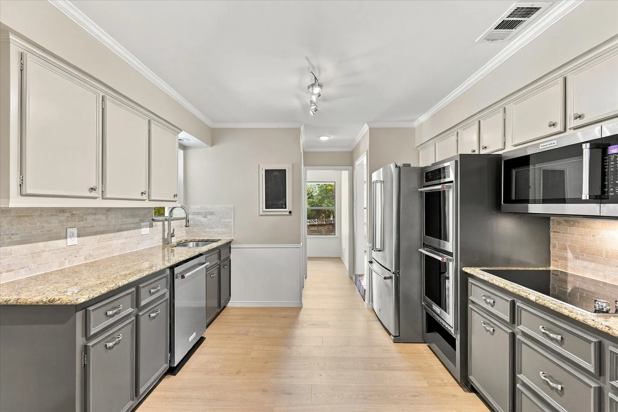 Well-appointed kitchen featuring dual-tone cabinetry, stone countertops, stainless steel appliances, and wood-finish flooring