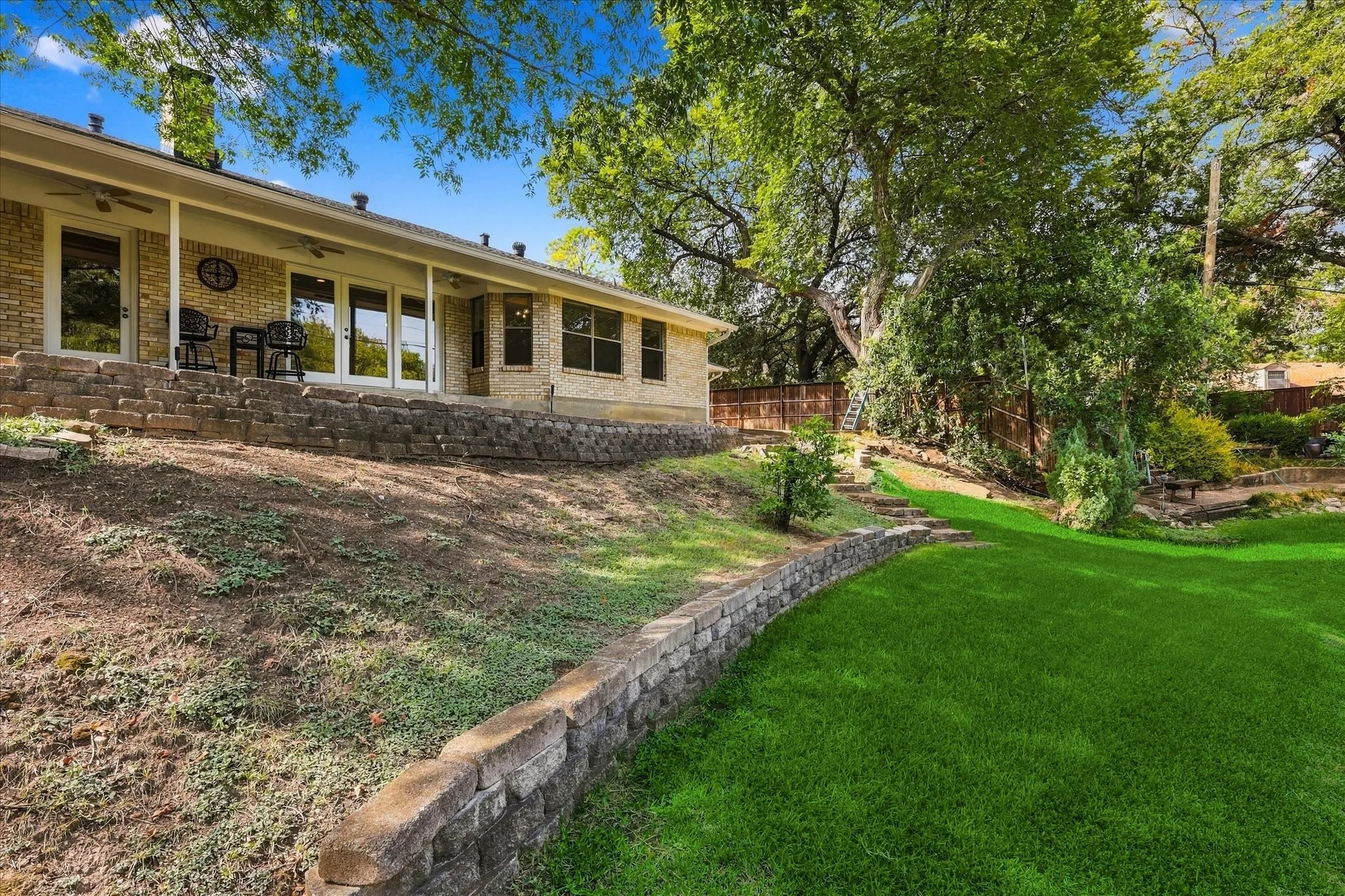 Brick exterior with covered patio, multiple glass panel doors, and tiered landscaping
