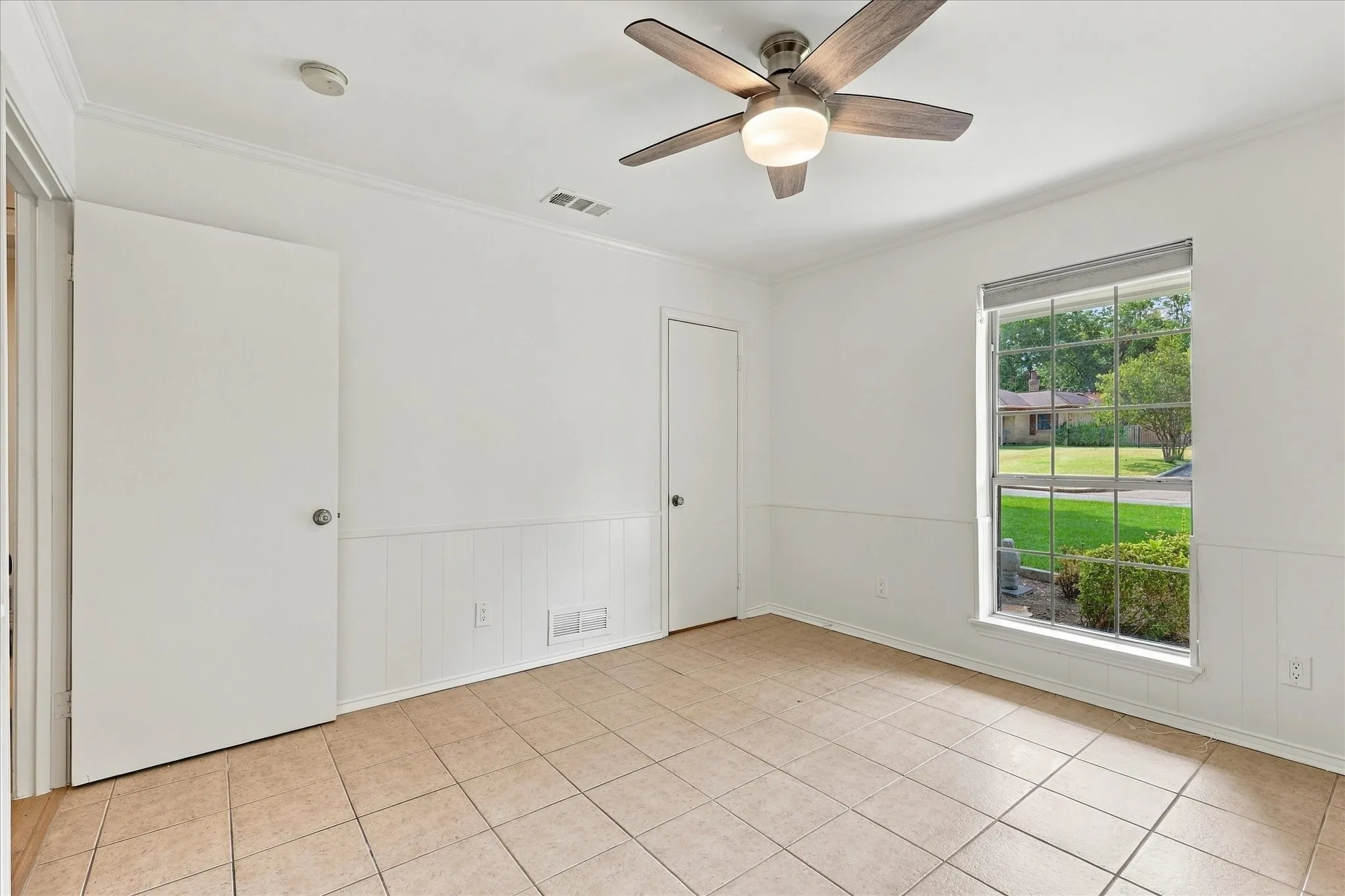 Tile flooring, white paneled wainscoting, ceiling fan with integrated lighting, crown molding, and a large window