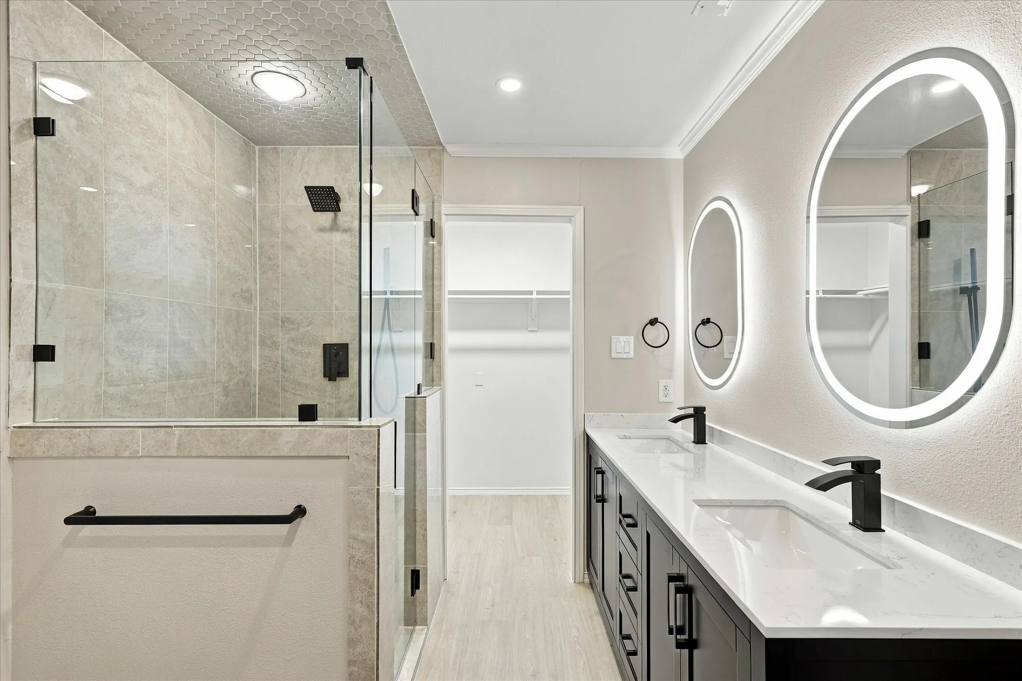 Walk-in shower with full-height glass enclosure, dual vanity with quartz countertops, and illuminated oval mirrors