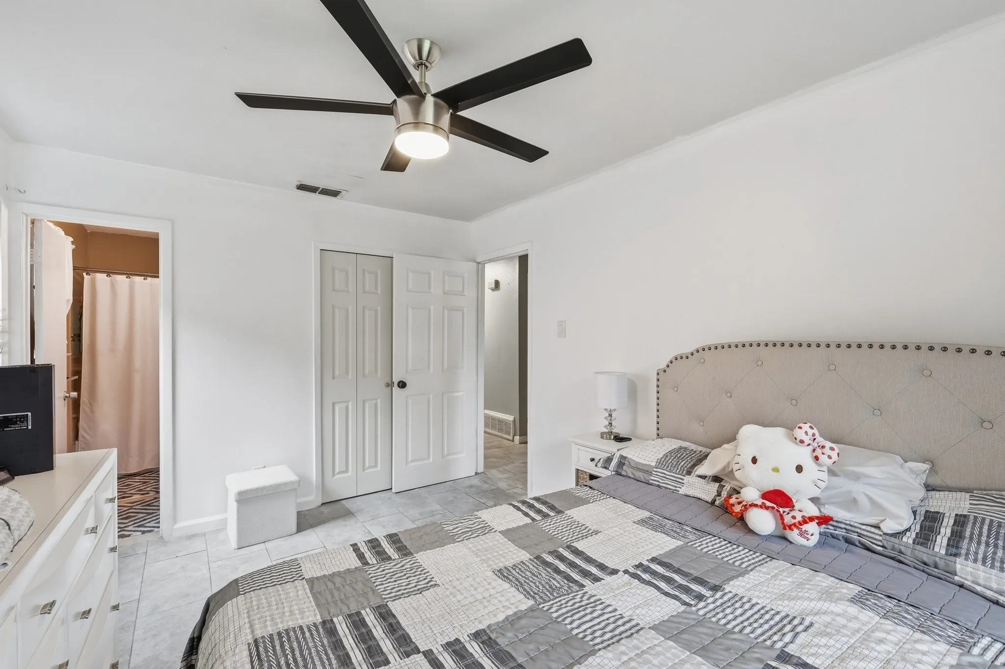 Ceiling fan with integrated lighting, tile flooring, white walls, and a tufted headboard