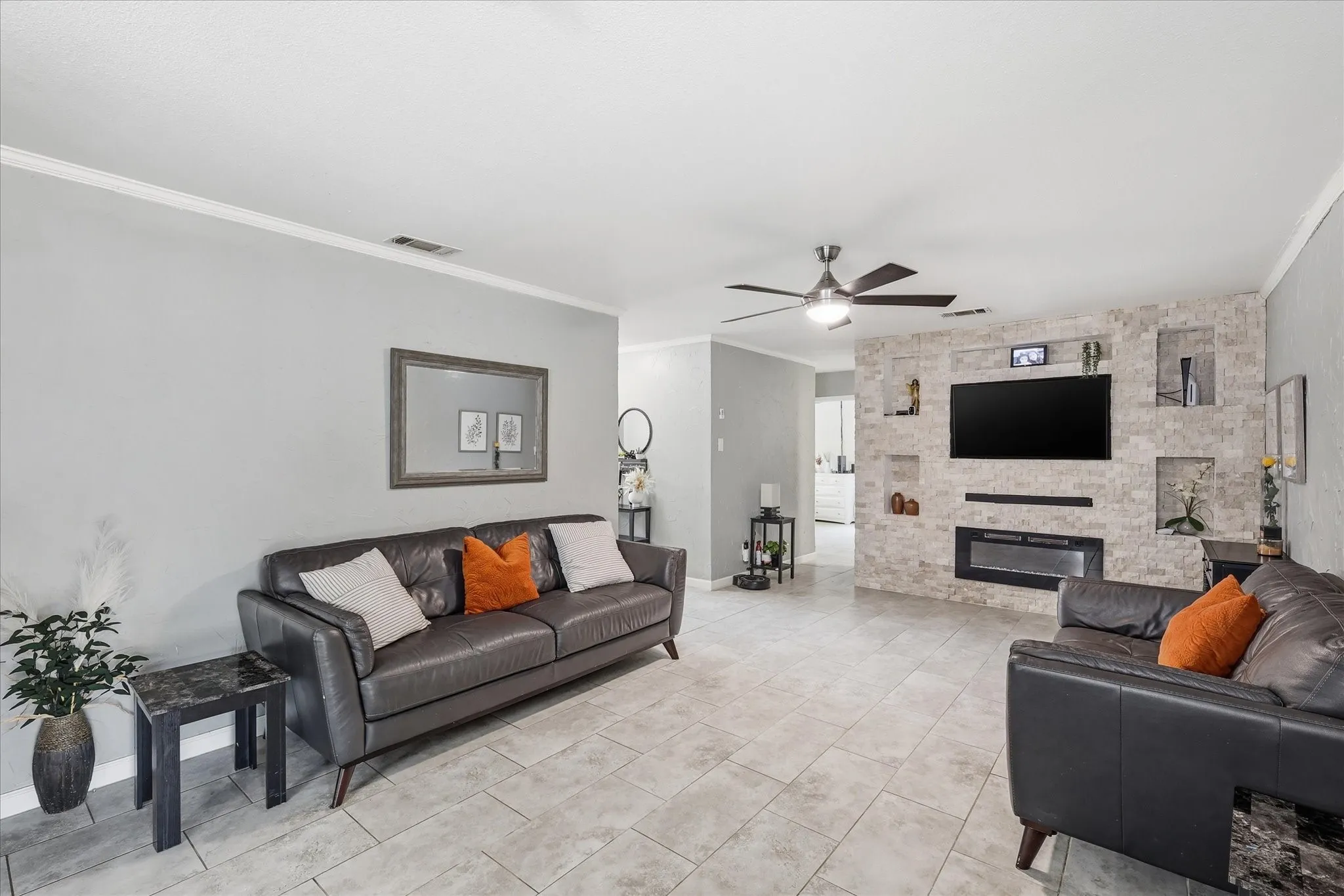 Spacious living area featuring tile flooring, crown molding, a ceiling fan, and a stone accent wall with an integrated electric fireplace and recessed display niches