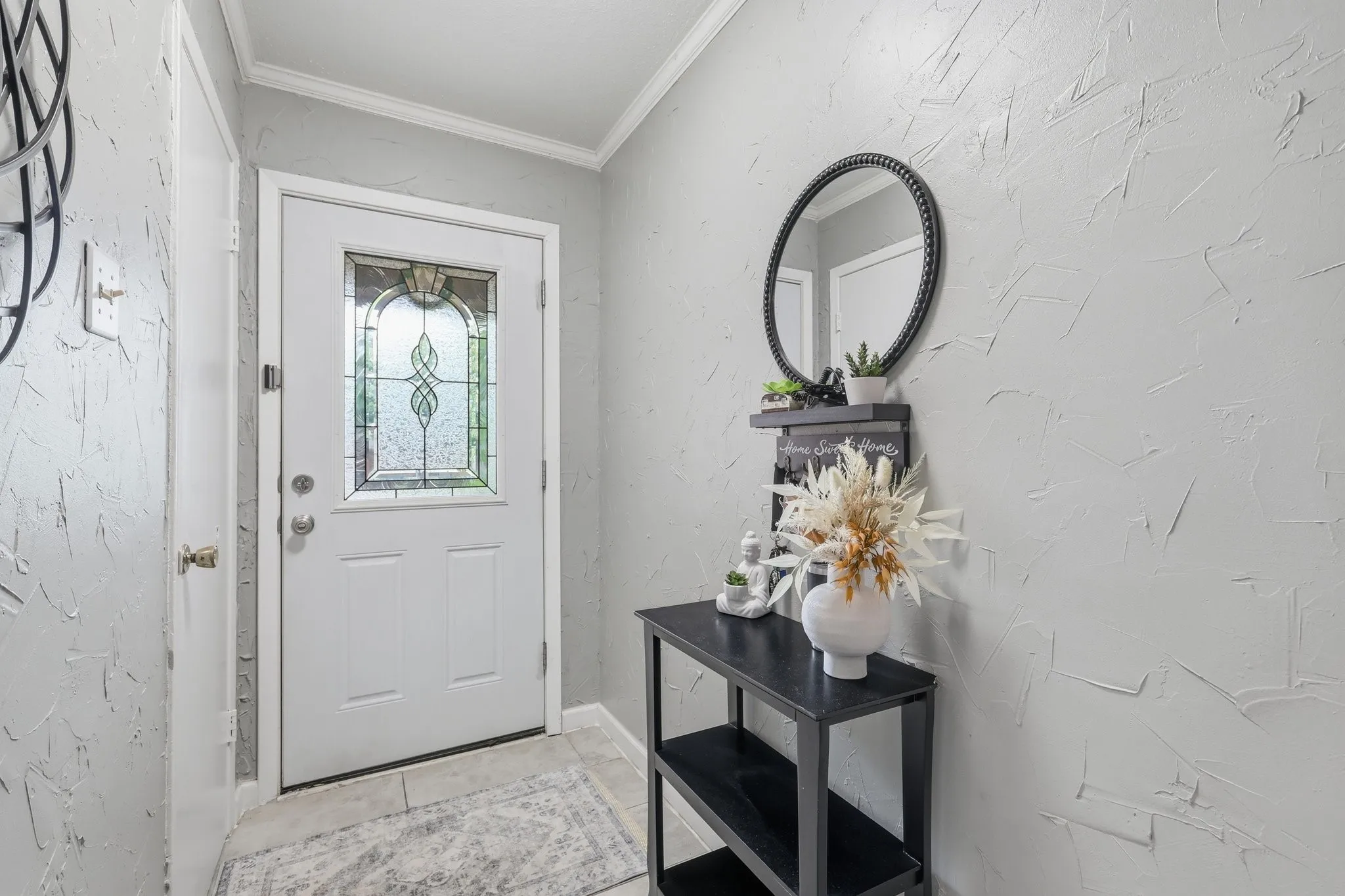 Entryway featuring a white door with decorative glass, light gray textured walls, crown molding, and tiled flooring