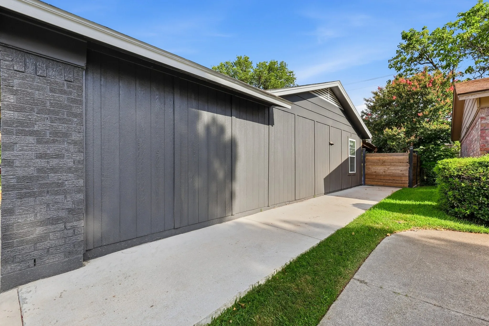 Exterior featuring dark gray vertical siding, dark gray brick accents, light gray roofline trim, concrete walkway, and a partial wooden fence