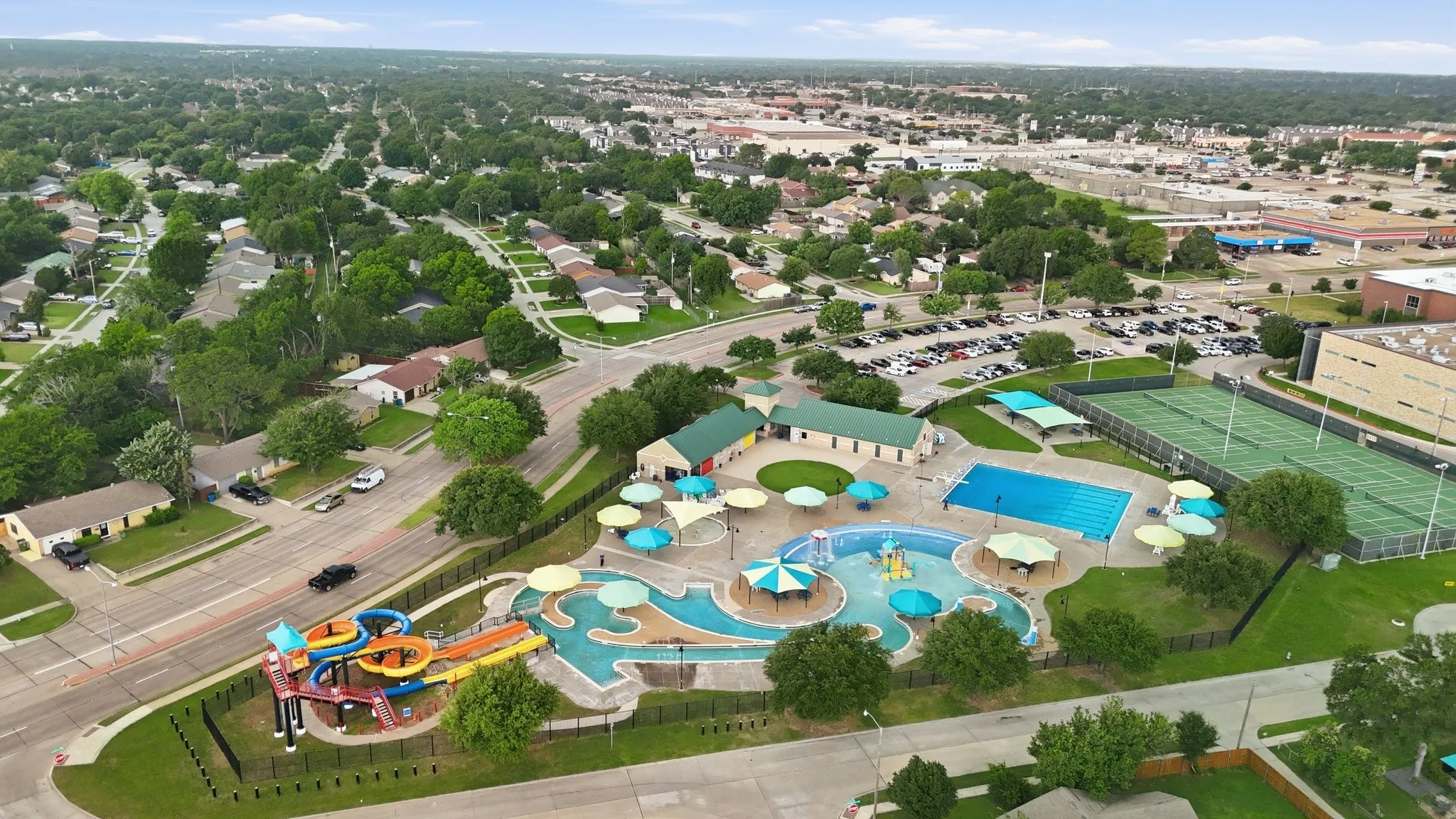 Outdoor community pool, adjacent water park with slides, tennis courts, and surrounding residential area