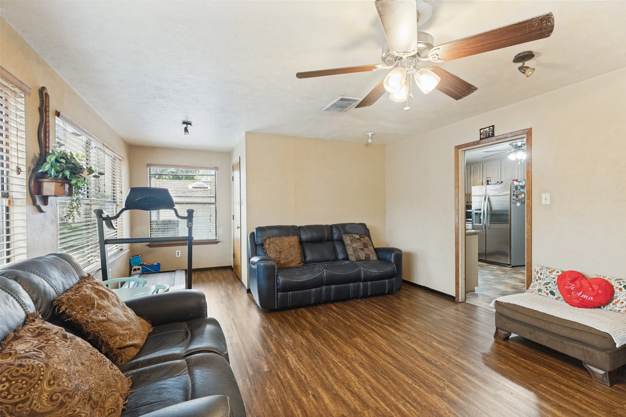 Wood-finish flooring, ceiling fan with integrated lighting, multiple windows with blinds, track lighting, and a framed doorway