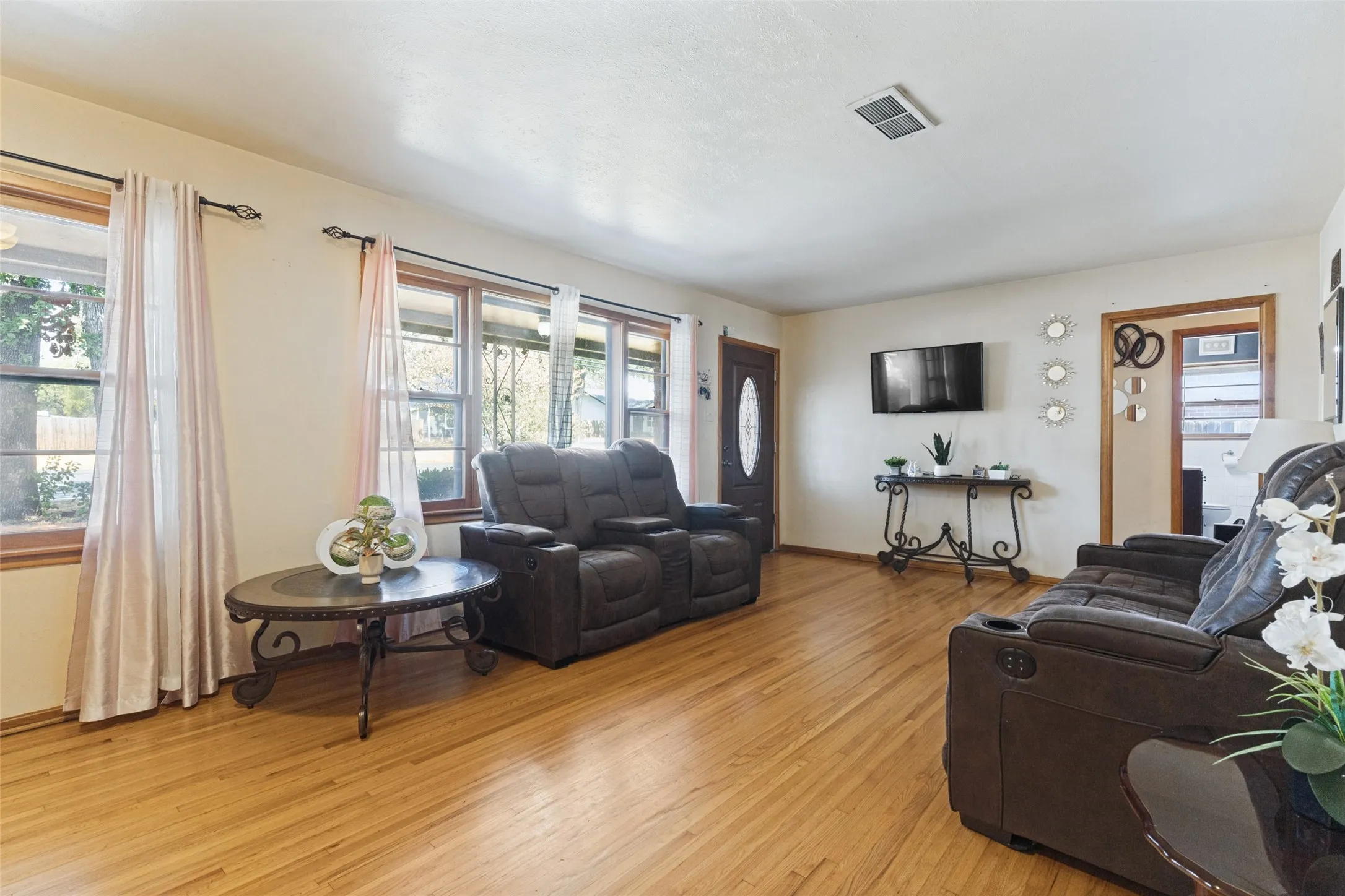 Wood-finish flooring throughout, multiple windows with wood trim, and a paneled entry door with an oval glass insert