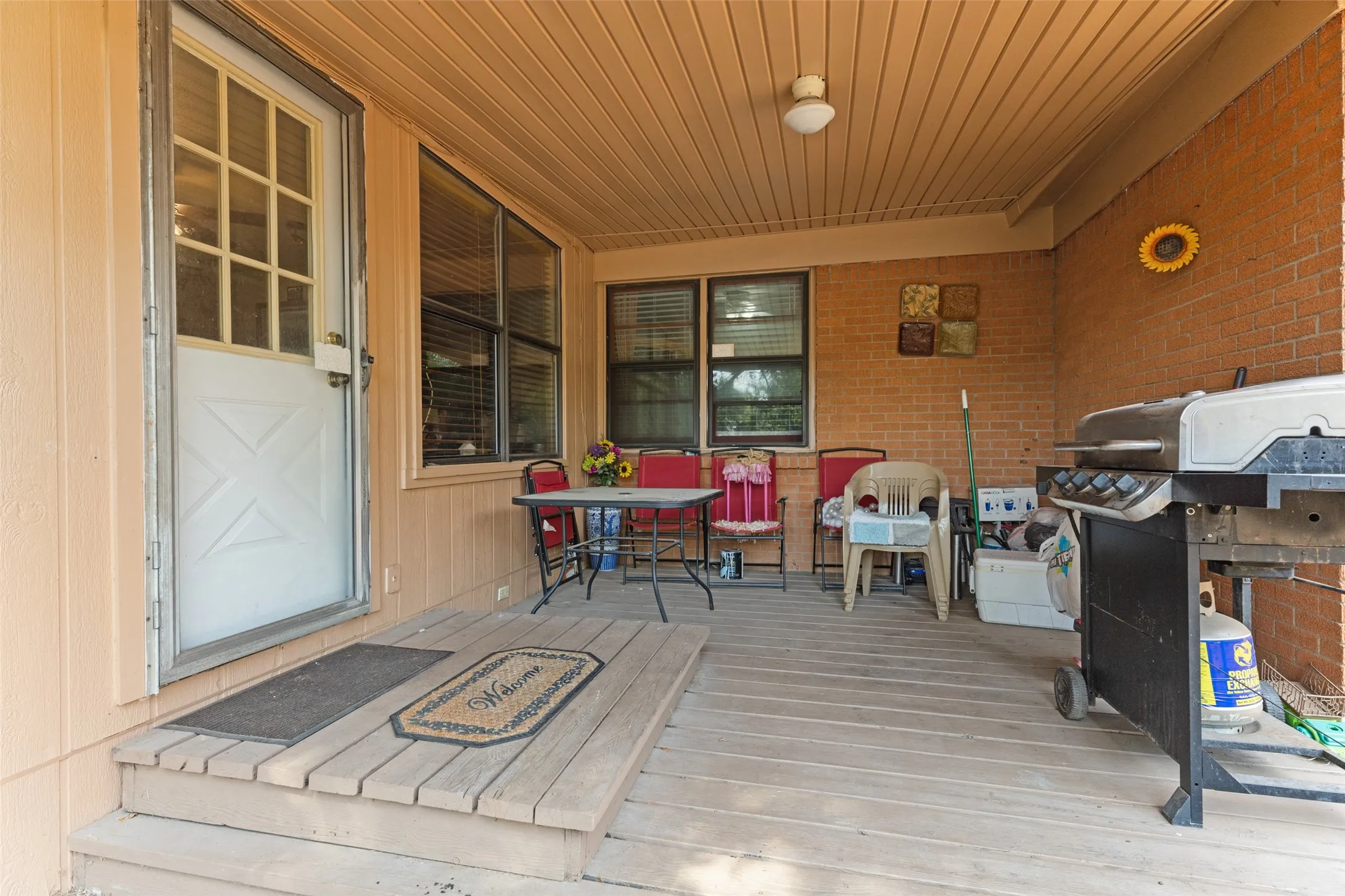 Covered porch with wood plank flooring, beadboard ceiling, and brick exterior wall
