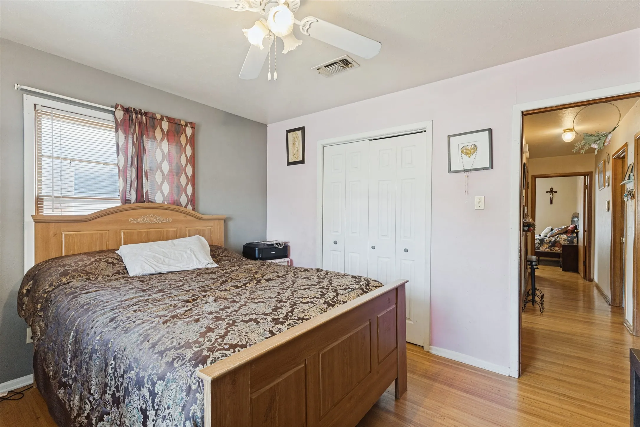 Ceiling fan with light fixture, window with blinds, bi-fold closet doors, and hardwood flooring
