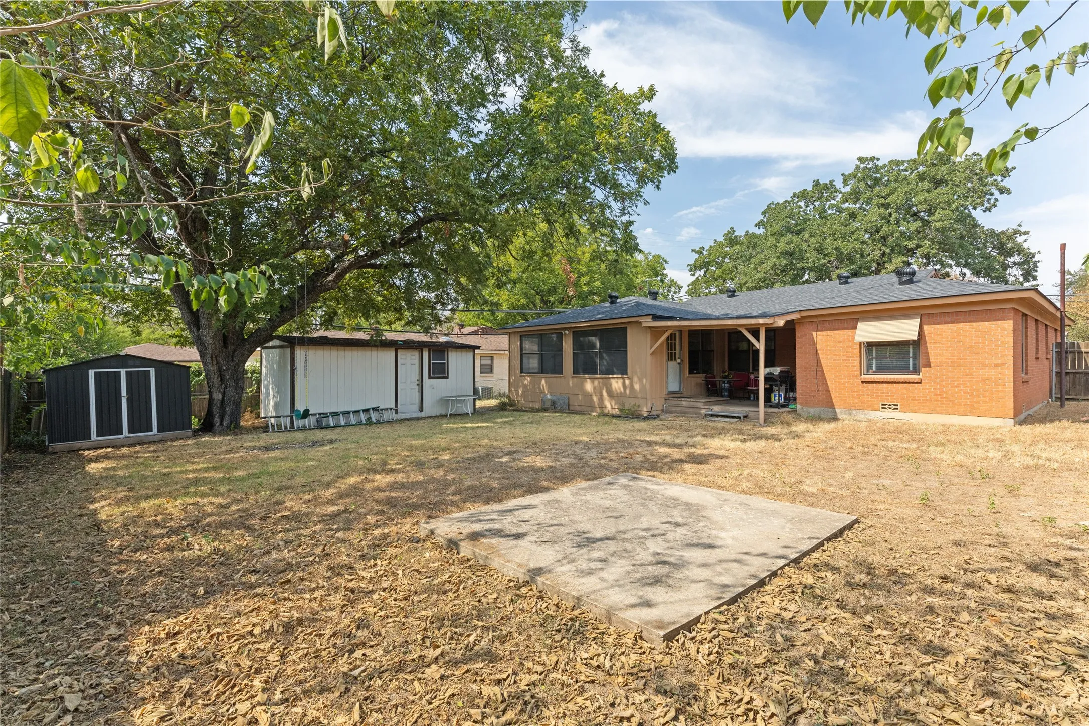 Expansive backyard featuring a brick exterior, covered patio, and a separate storage shed