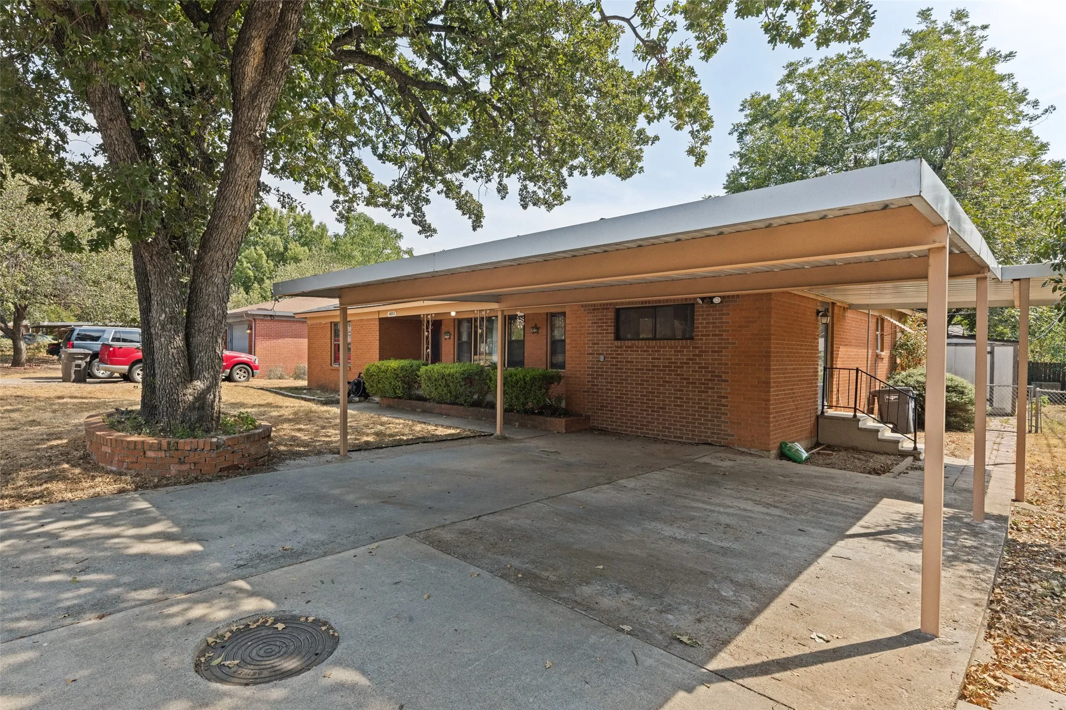 Brick exterior with a covered carport, mature trees, and concrete driveway