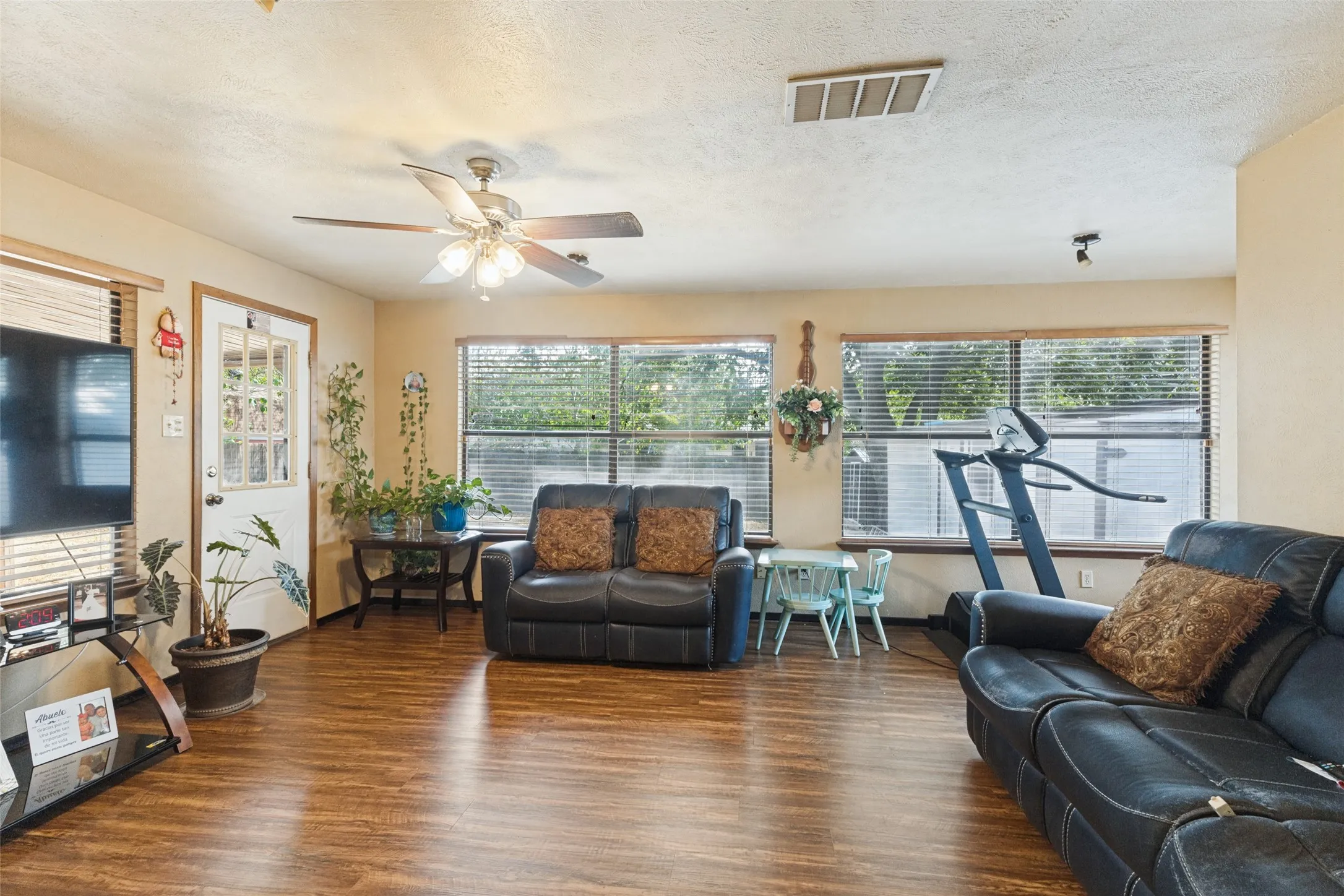 Wood-finish flooring throughout, ceiling fan with integrated lighting, multiple windows with blinds, and white panel door with glass inserts