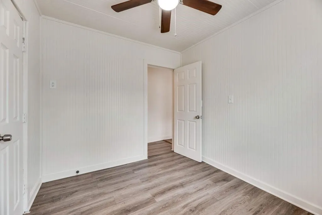 Wood-finish plank flooring, white beadboard walls, and a ceiling fan with integrated lighting