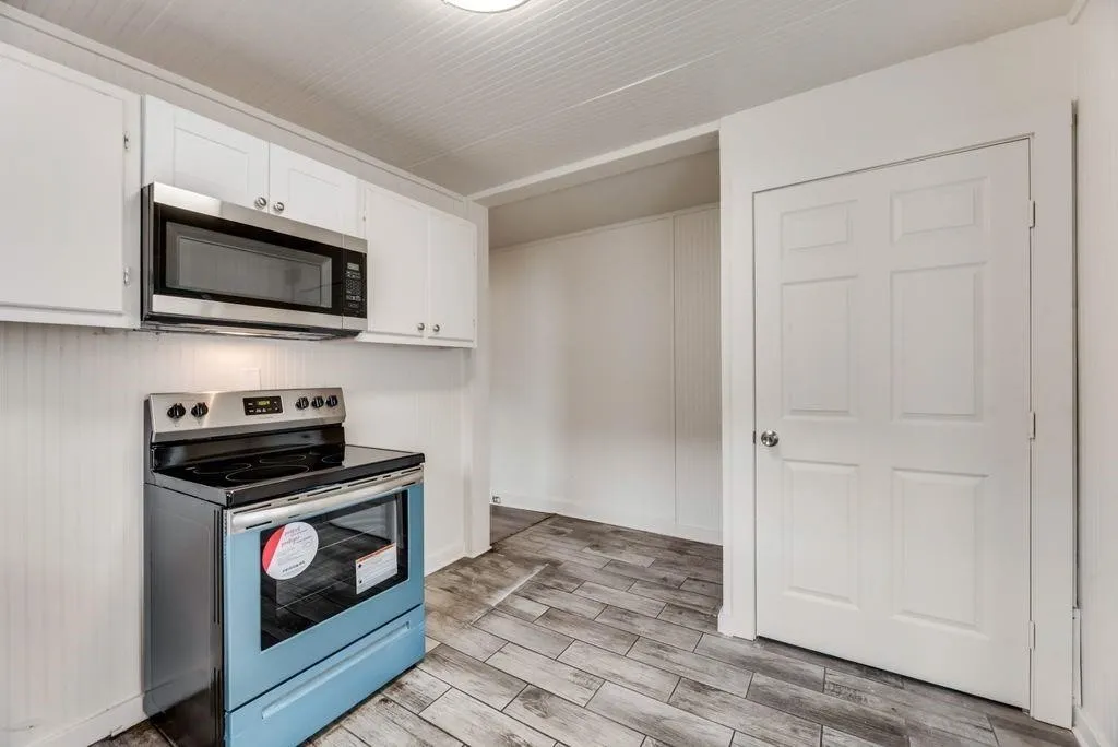 Stainless steel microwave and range, white cabinetry, beadboard wainscoting, panel door, and wood-finish flooring