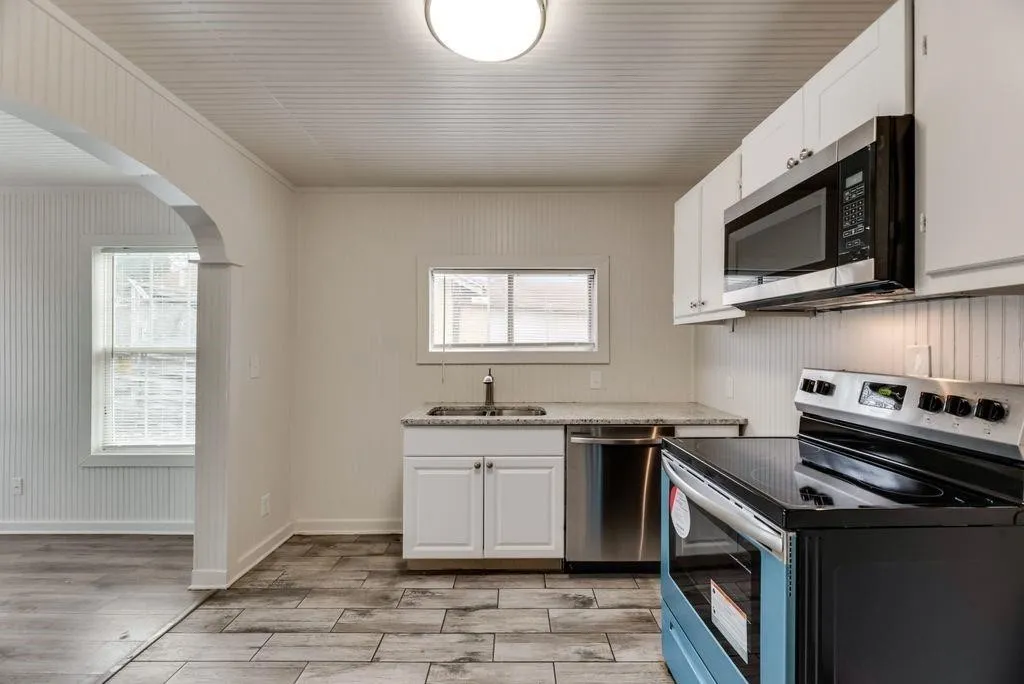 White cabinetry, stainless steel appliances, wood-finish flooring, beadboard wall paneling, and a kitchen archway